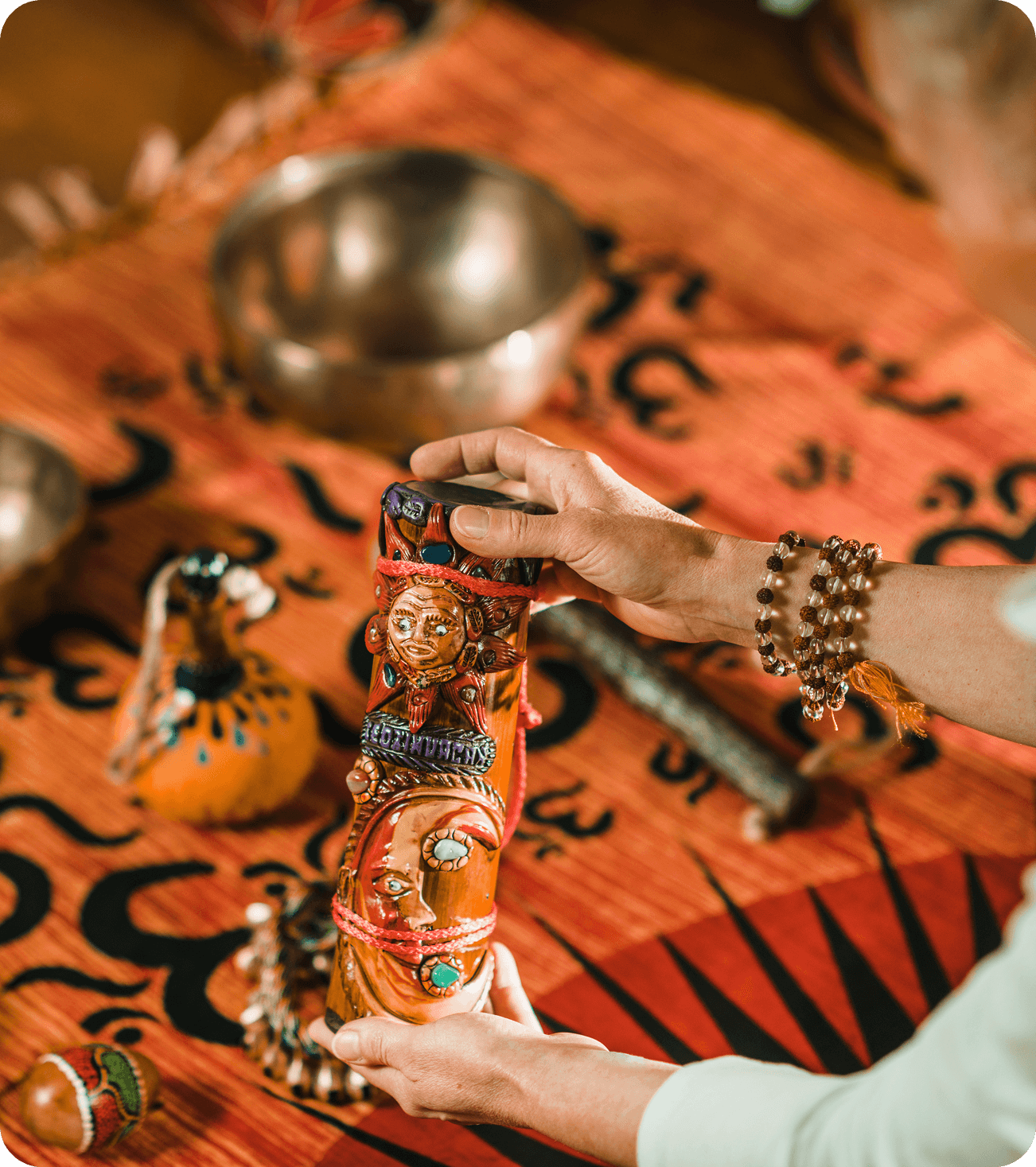 Hands holding a handcrafted Indian tribal wooden art piece with face carvings and bead embellishments.