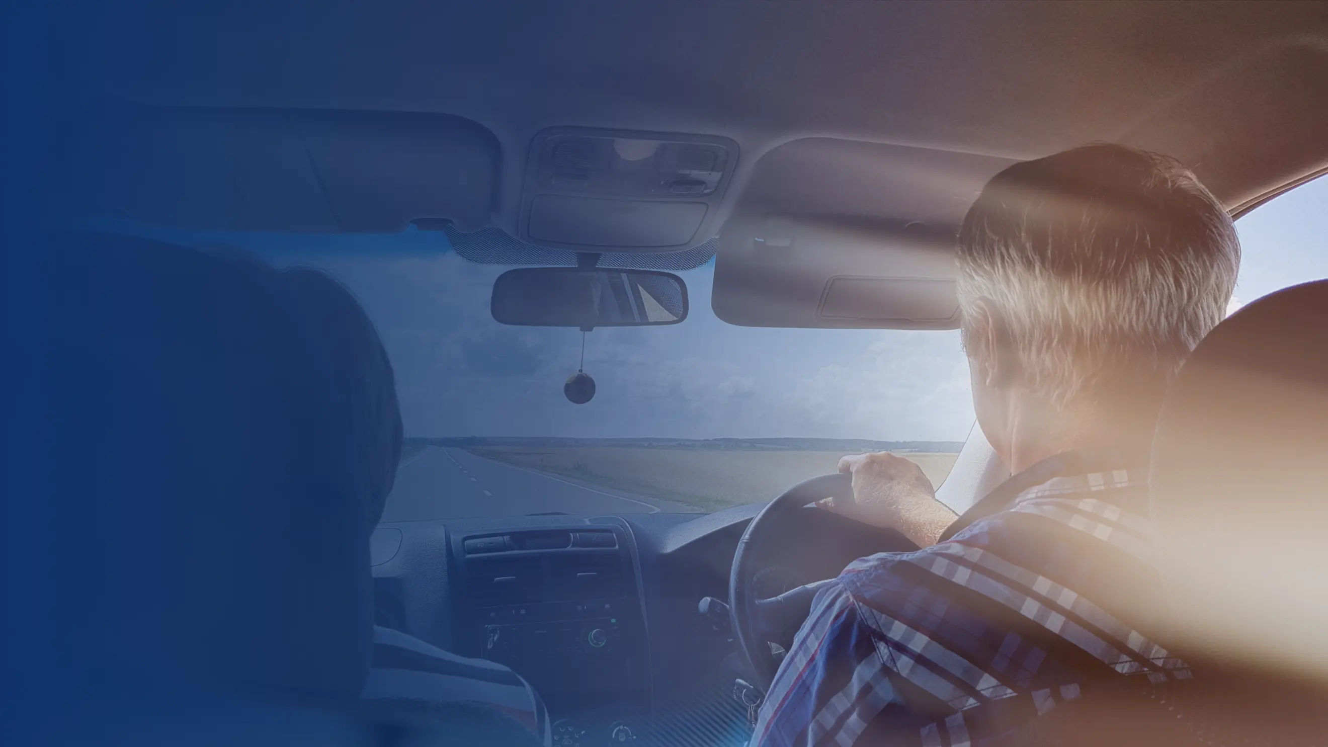 View from the back seat of an older man driving a car on an open rural road, with a blue overlay