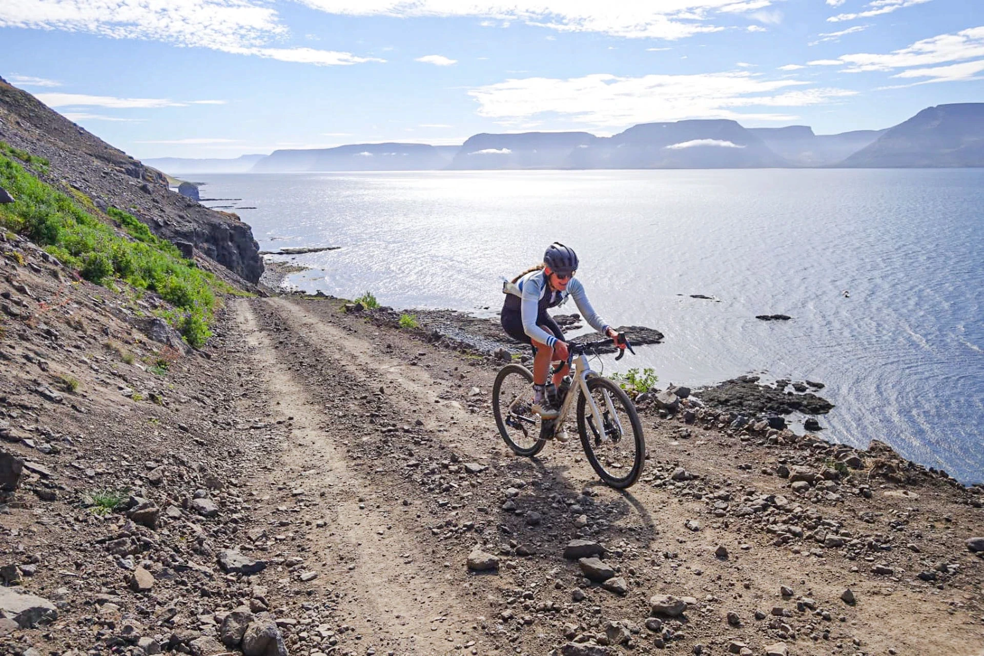 One gravel bike rider bikes towards camera with a fjord in backround