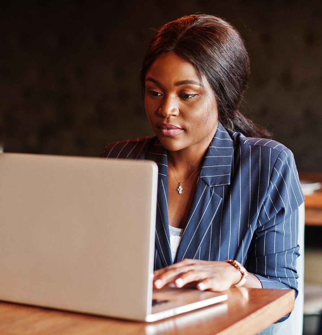 A professional woman in a business suit is focused on her laptop, engaged in work or a virtual meeting.