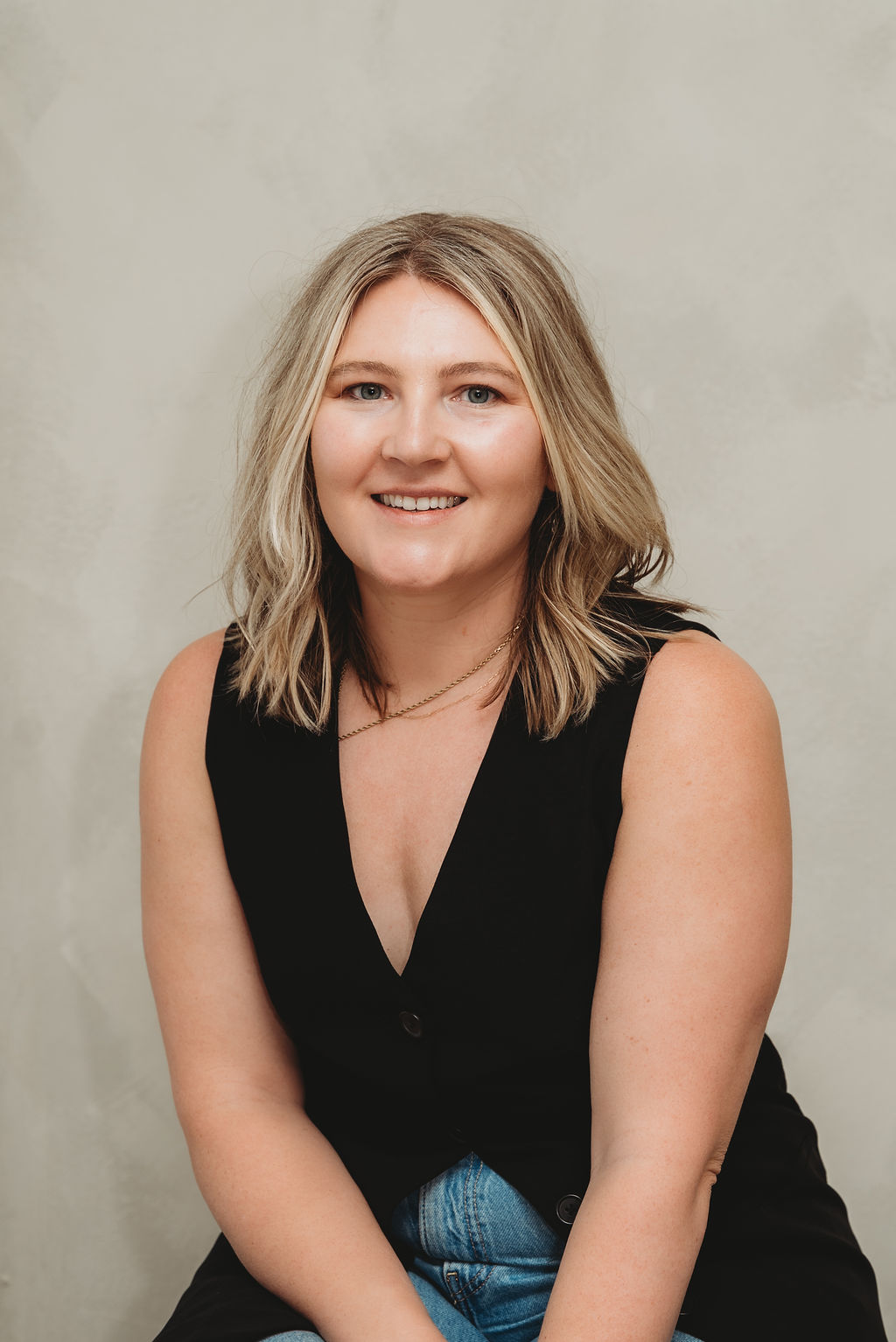 A woman with short, curly hair, wearing round glasses and a white t-shirt, smiling.