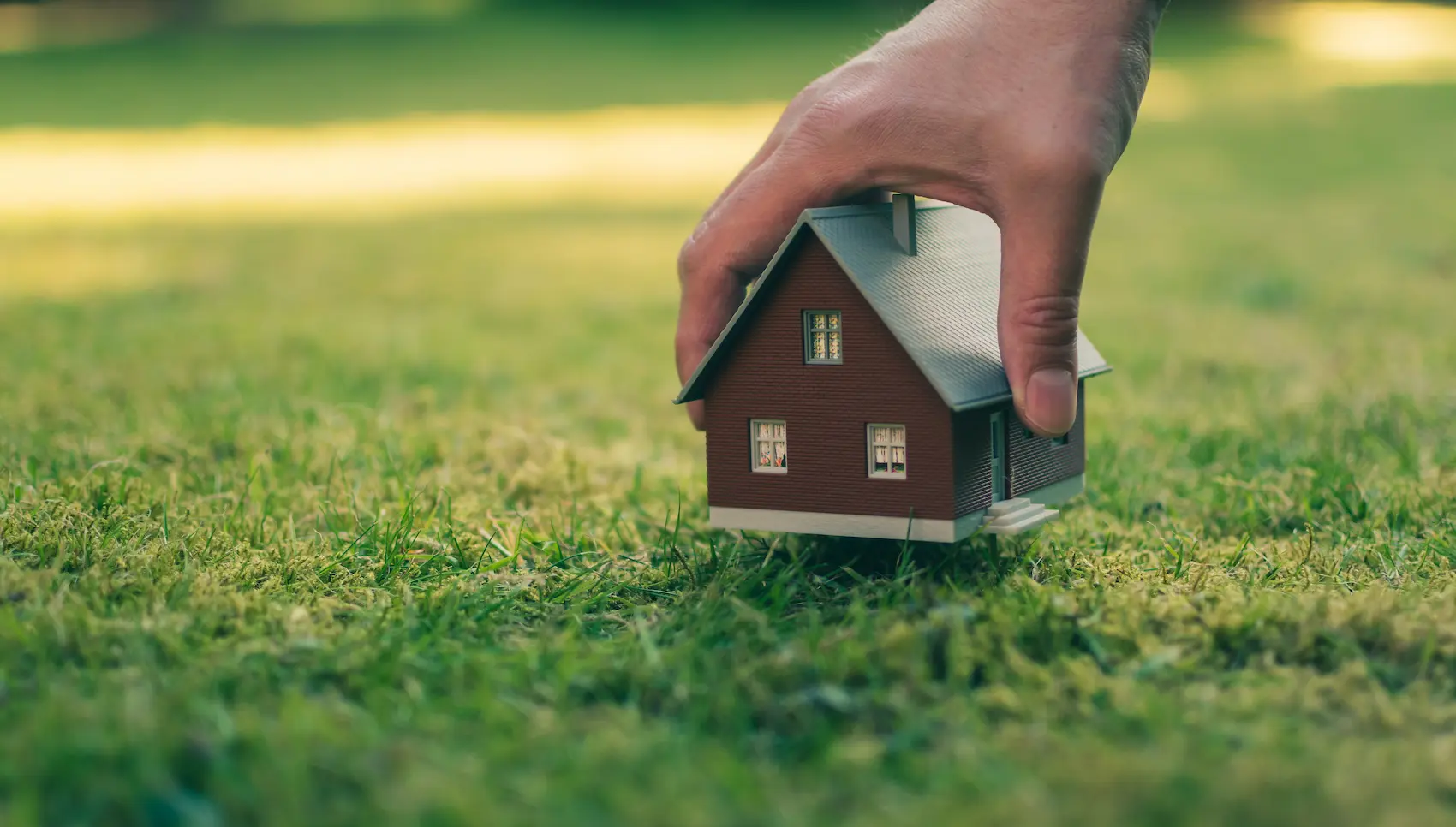 Kleines Hausmodell auf grünem Rasen als Symbol für erfolgreichen Immobilienverkauf