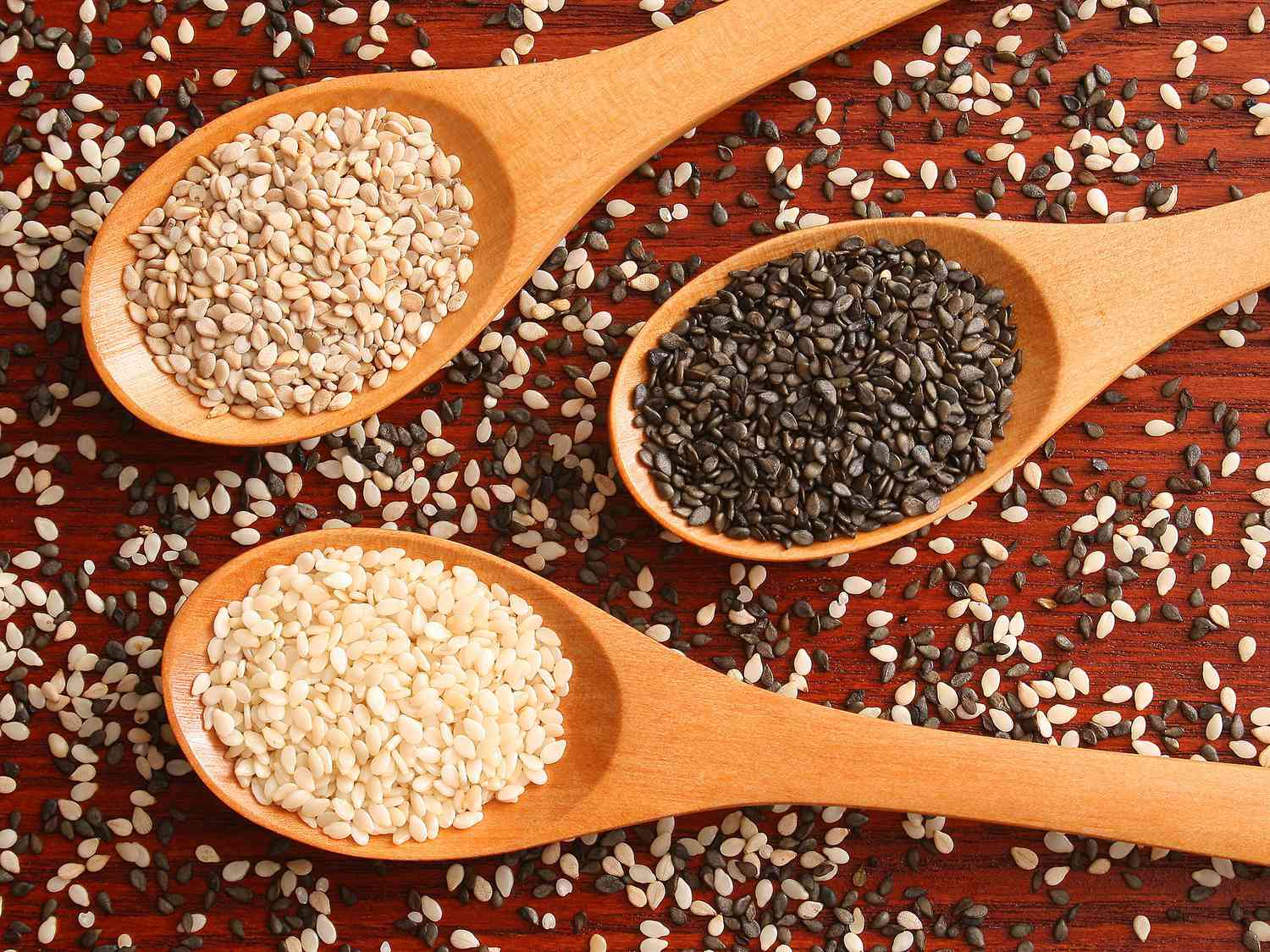 white, black and brown colour sesame seeds in three different wooden spoons