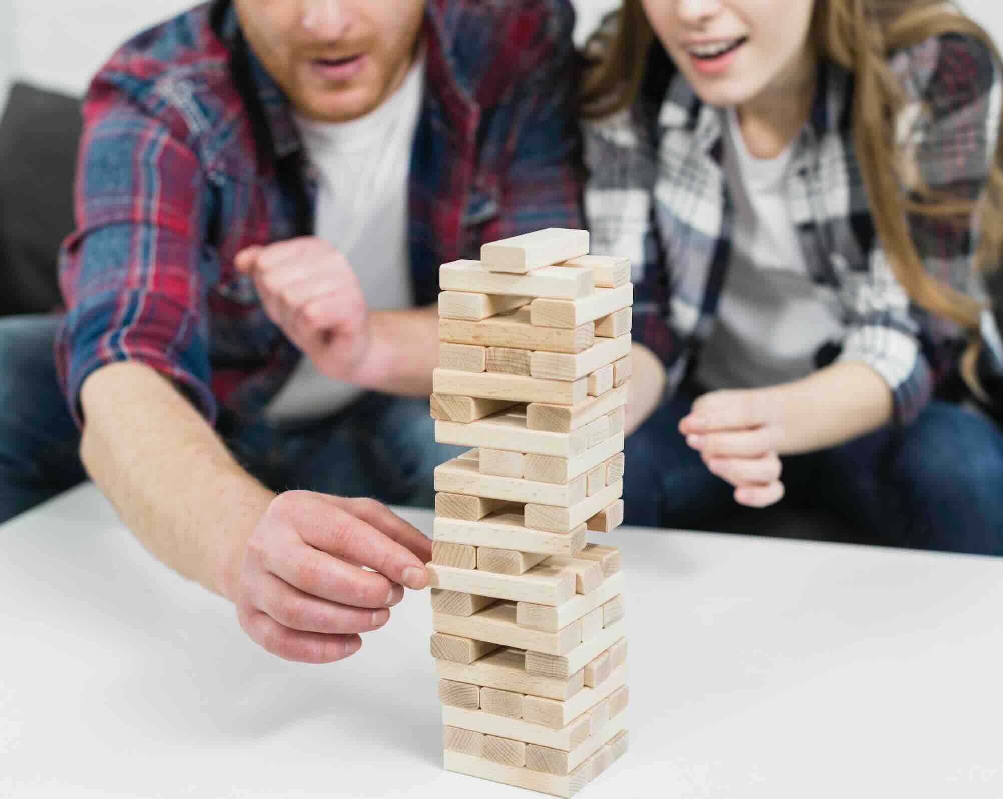 A man and a woman playing Jenga, carefully pulling out a block from a tall stack.