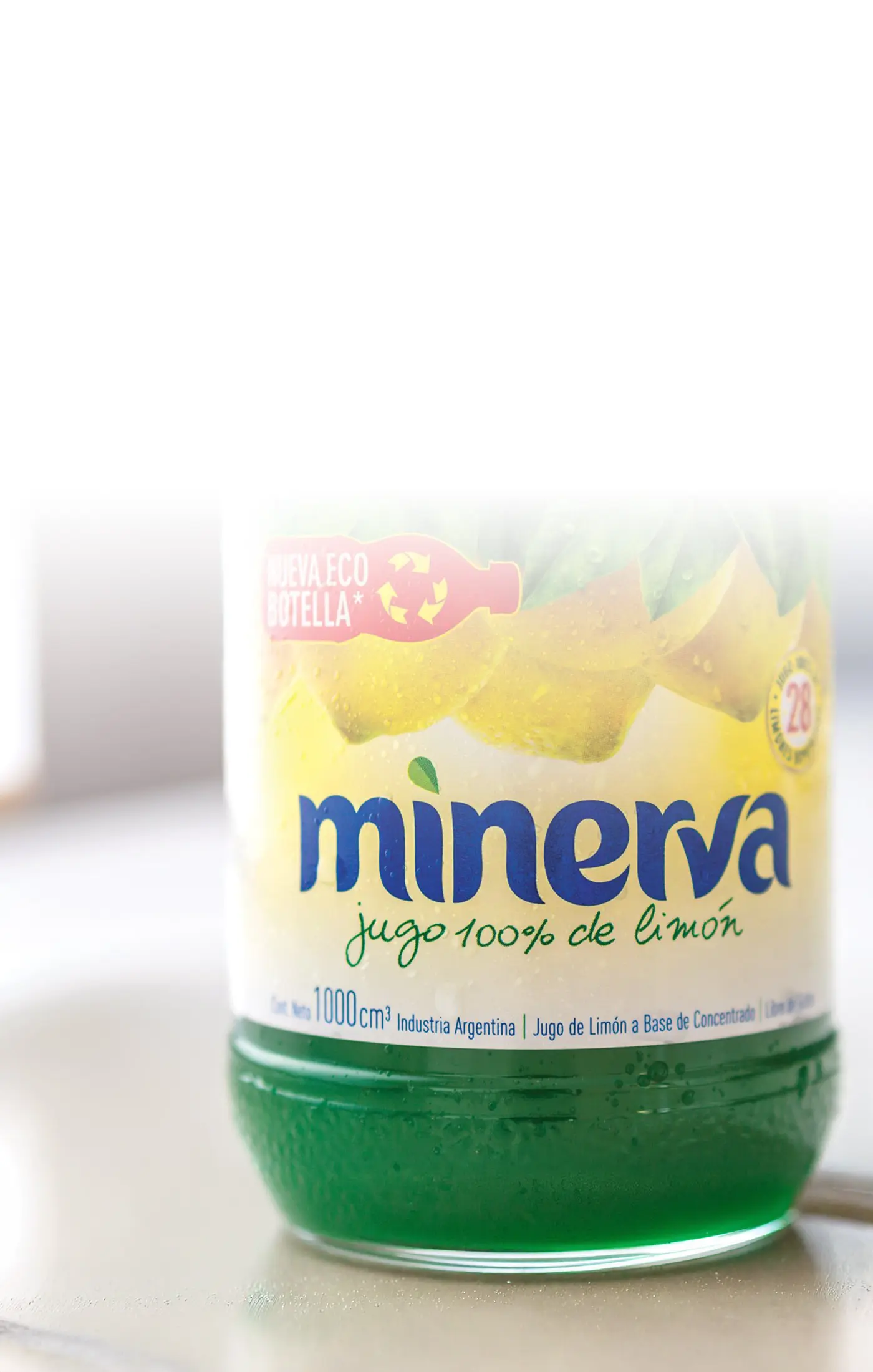 Close-up of a green Minerva lemon juice bottle with a label reading "jugo 100% de limón." The eco-friendly packaging and yellow lemon imagery are visible.