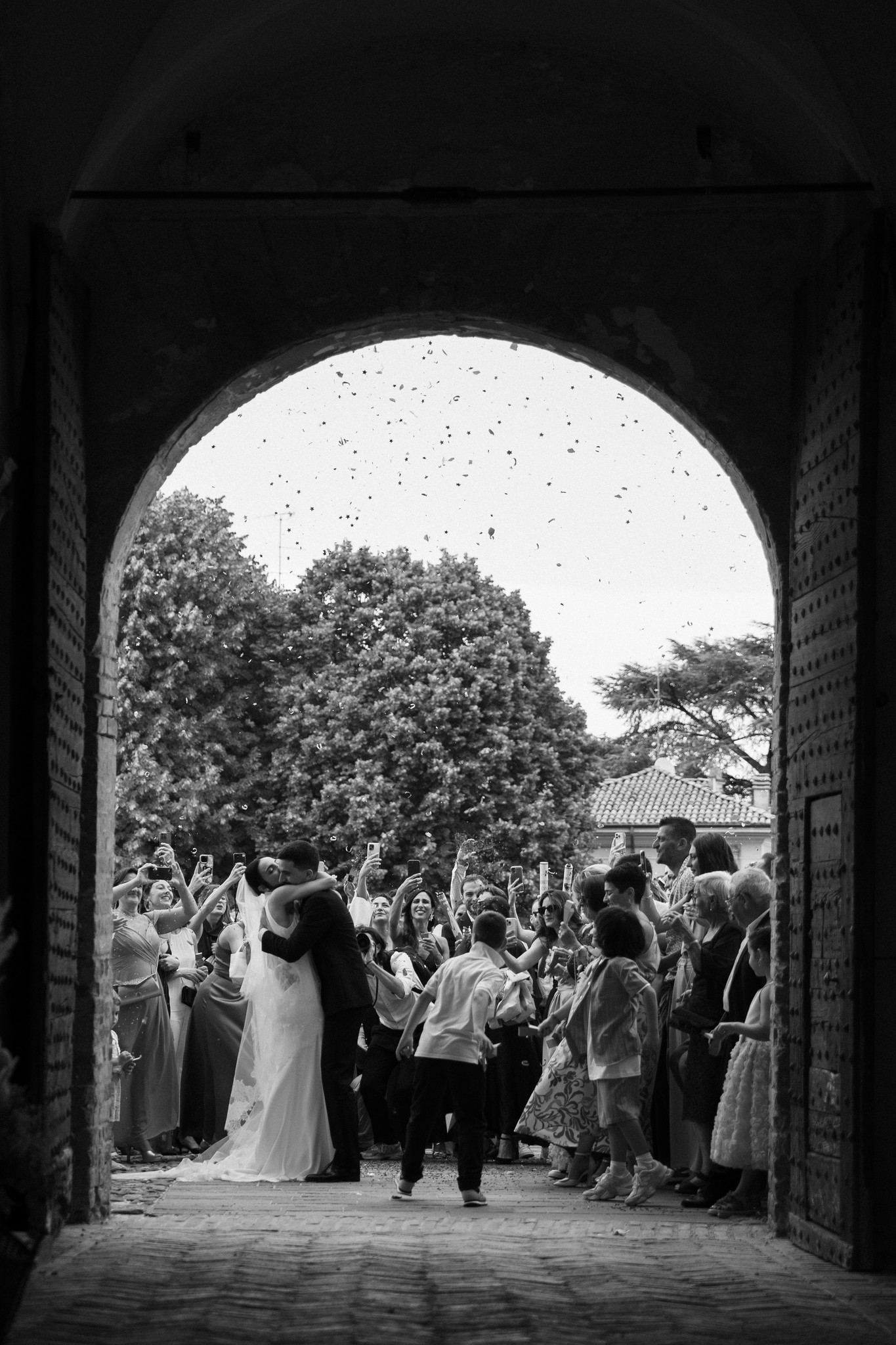 Sposi escono dall'arco in pietra mentre gli invitati applaudono nel giardino del Parco di Montebello, reportage di matrimonio