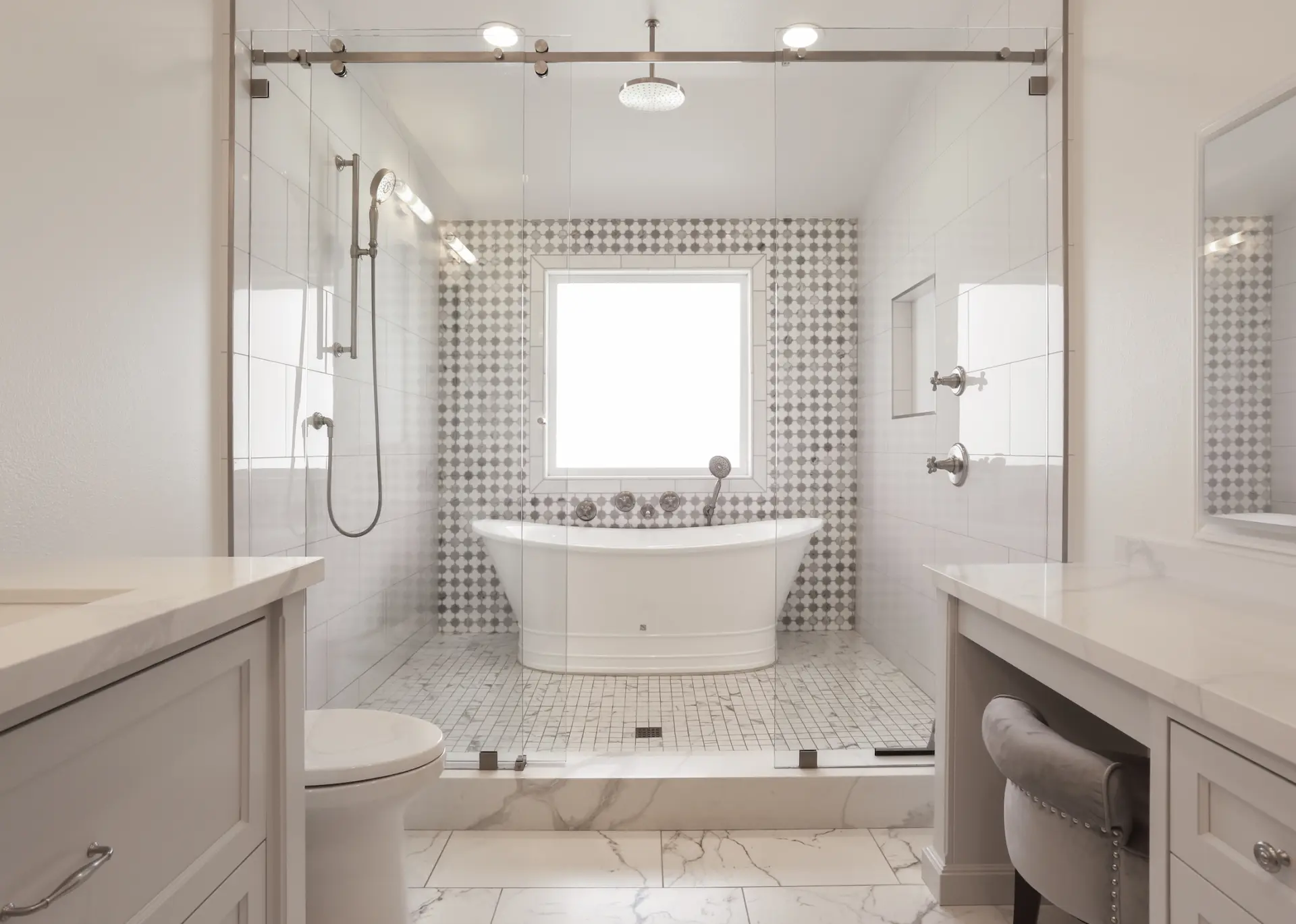 Straight view of primary bathroom with muted tones, double vanity, makeup vanity, and spacious walk-in shower and marble tile. Photo by Chris Darnall.