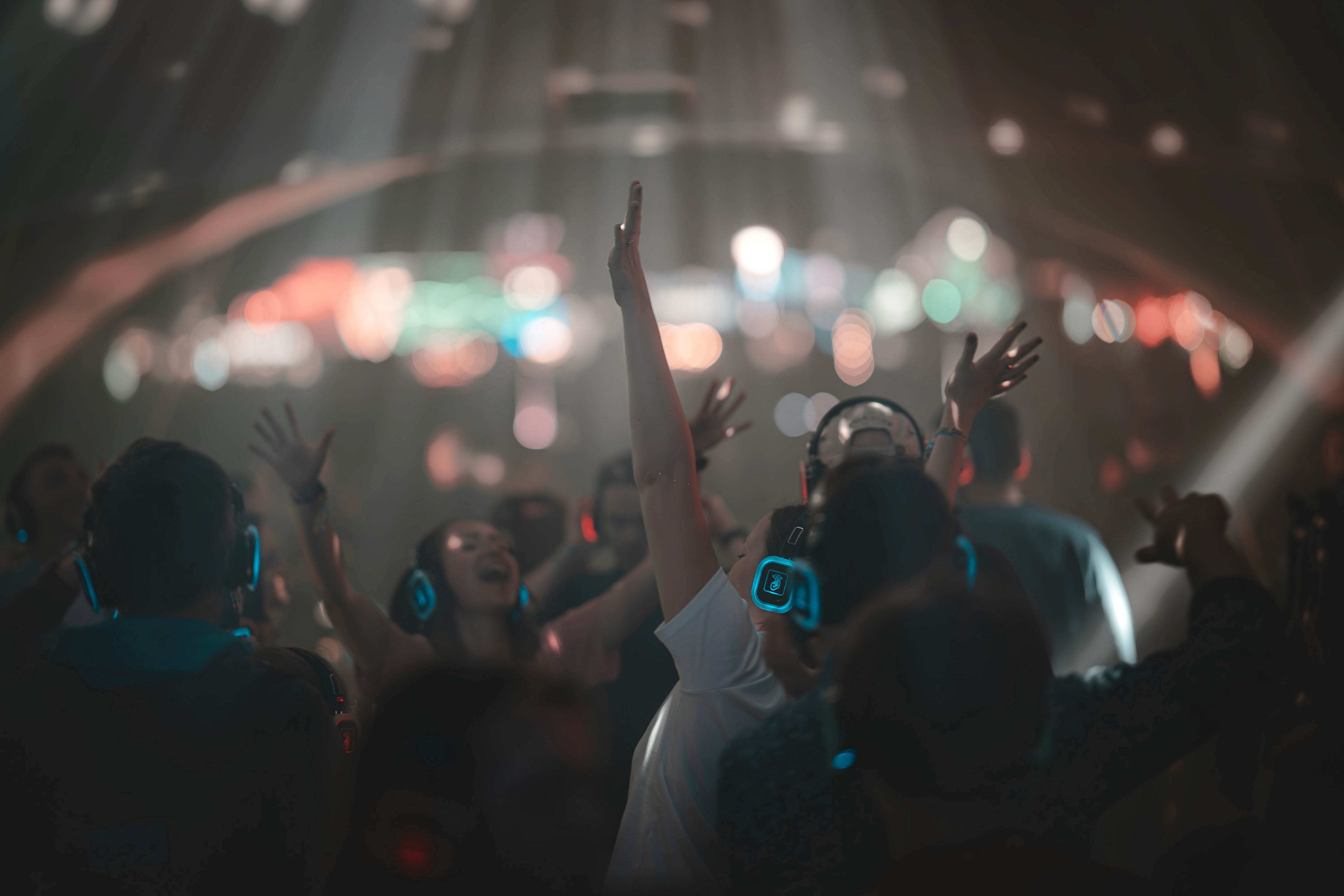 Festivalgoers dancing with wireless headphones under colorful lights at a silent disco.