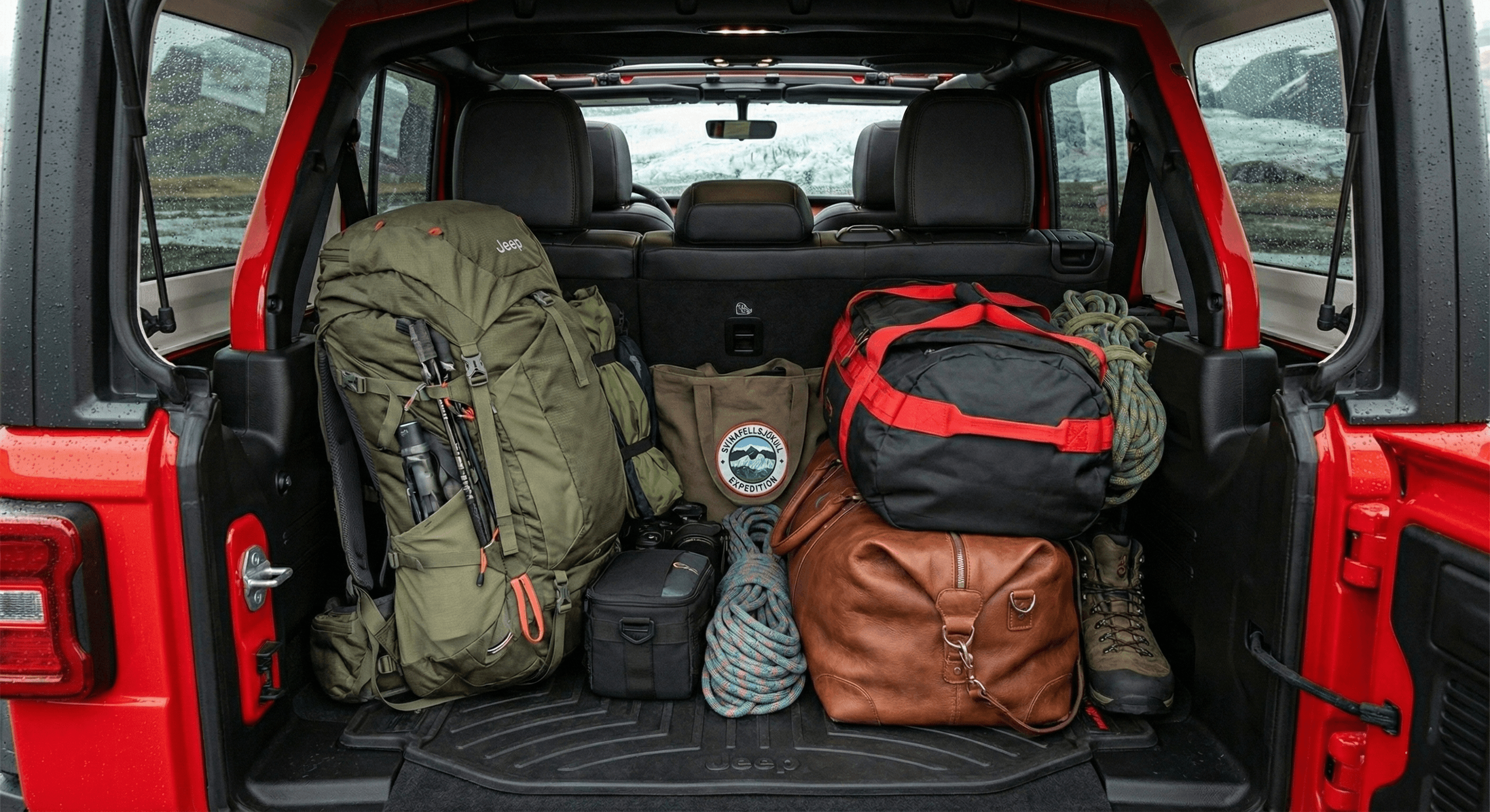 Rear view of a red Jeep with the trunk open, packed with hiking backpacks and bags.