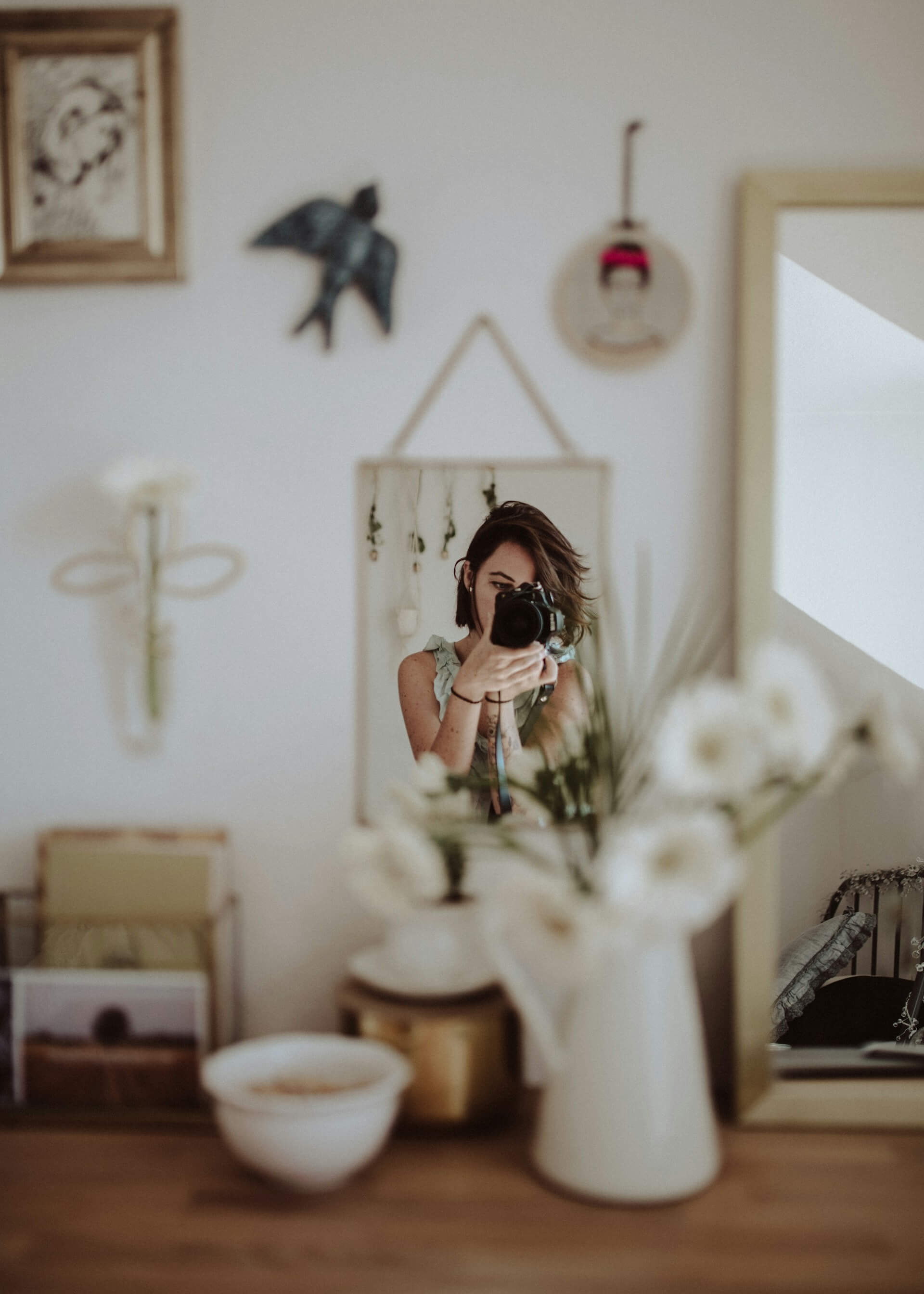 A woman captures a selfie while posing in front of a mirror, showcasing her smile and stylish outfit