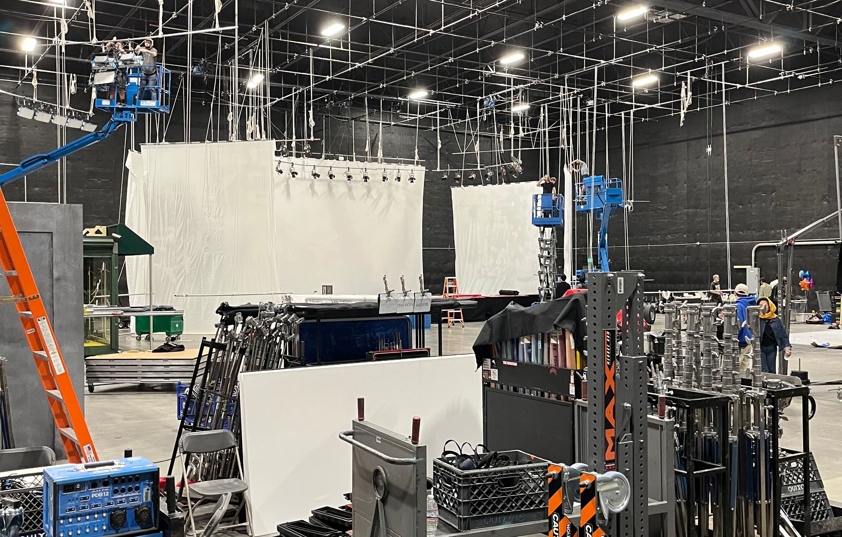 Grip carts staged on a large sound stage under an overhead pipe grid - a taco cart, milk-crate carts and a cart loaded with combo stands.