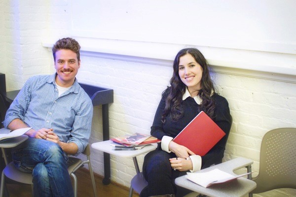 A photo of a man and a woman siting at some classroom desks.