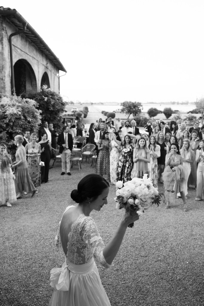 Sposa con bouquet bianco in piedi davanti agli ospiti nel giardino della villa, reportage di matrimonio in bianco e nero