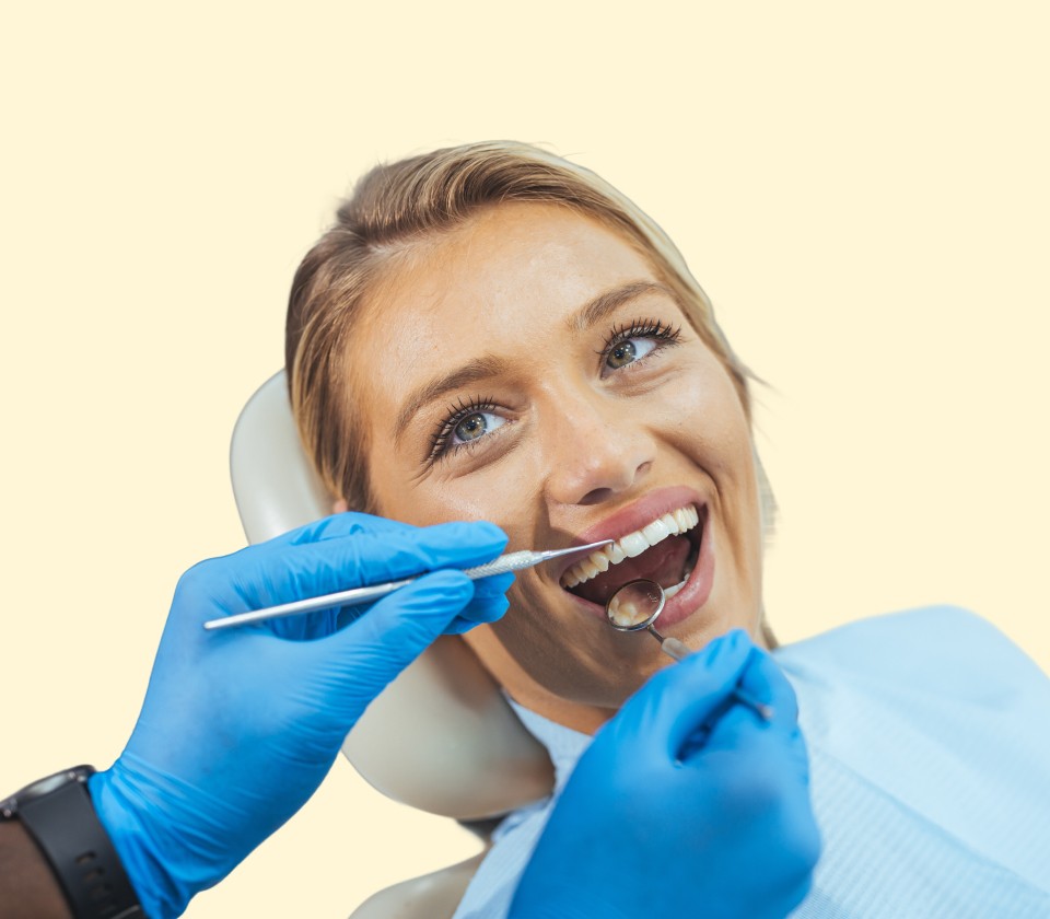 Kvinne smiler i tannlegestolen mens tannlegen utfører undersøkelse med speil og hansker.