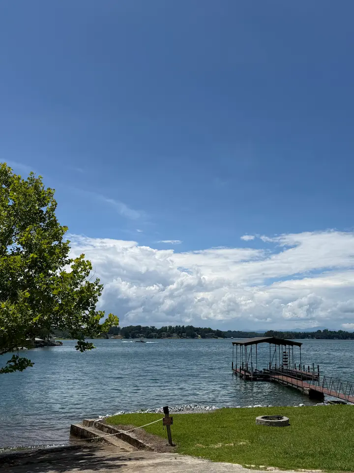 Boat dock on Lake Keowee with bright blue sky, clouds, and peaceful water reflecting a summer day.