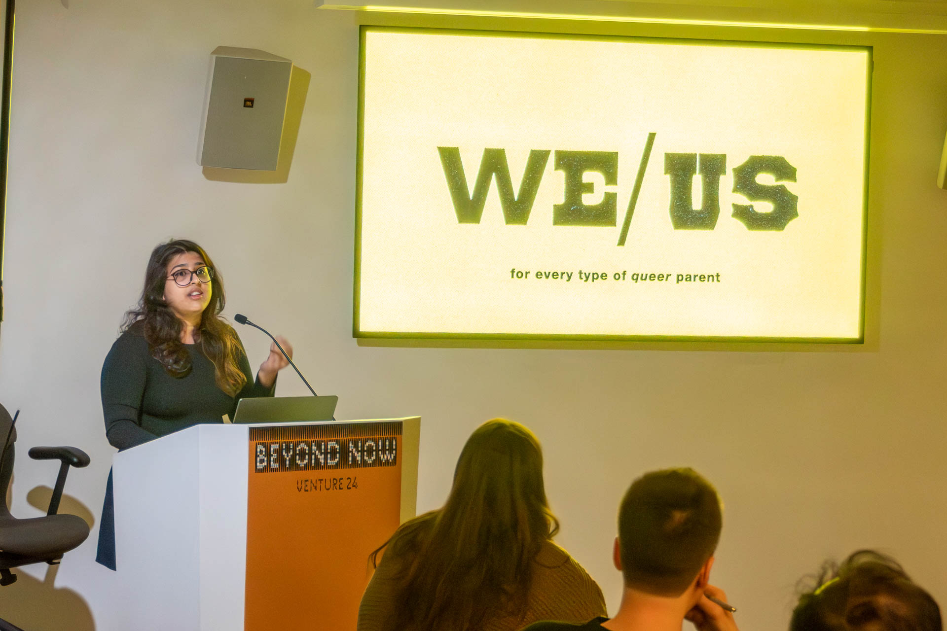 A lady at the podium giving a presentation to a class.
