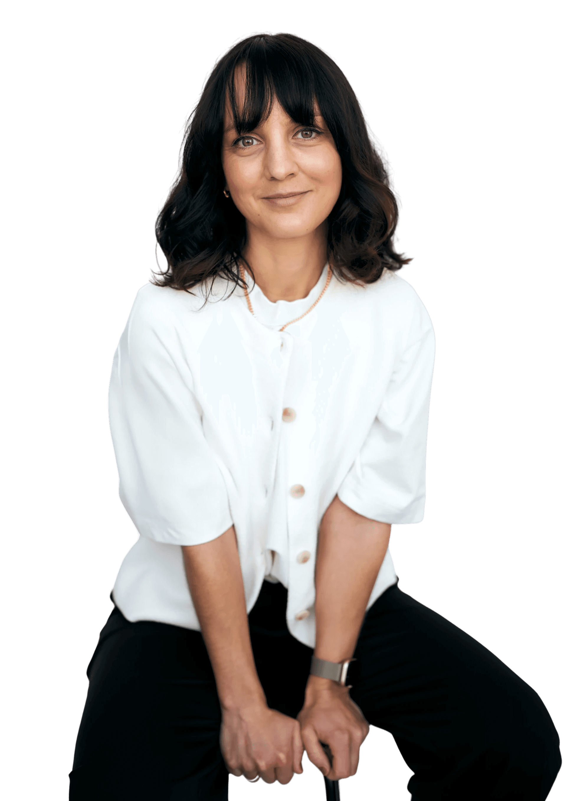 A young person with curly hair smiles at the camera while sitting in front of a laptop against a dark background.