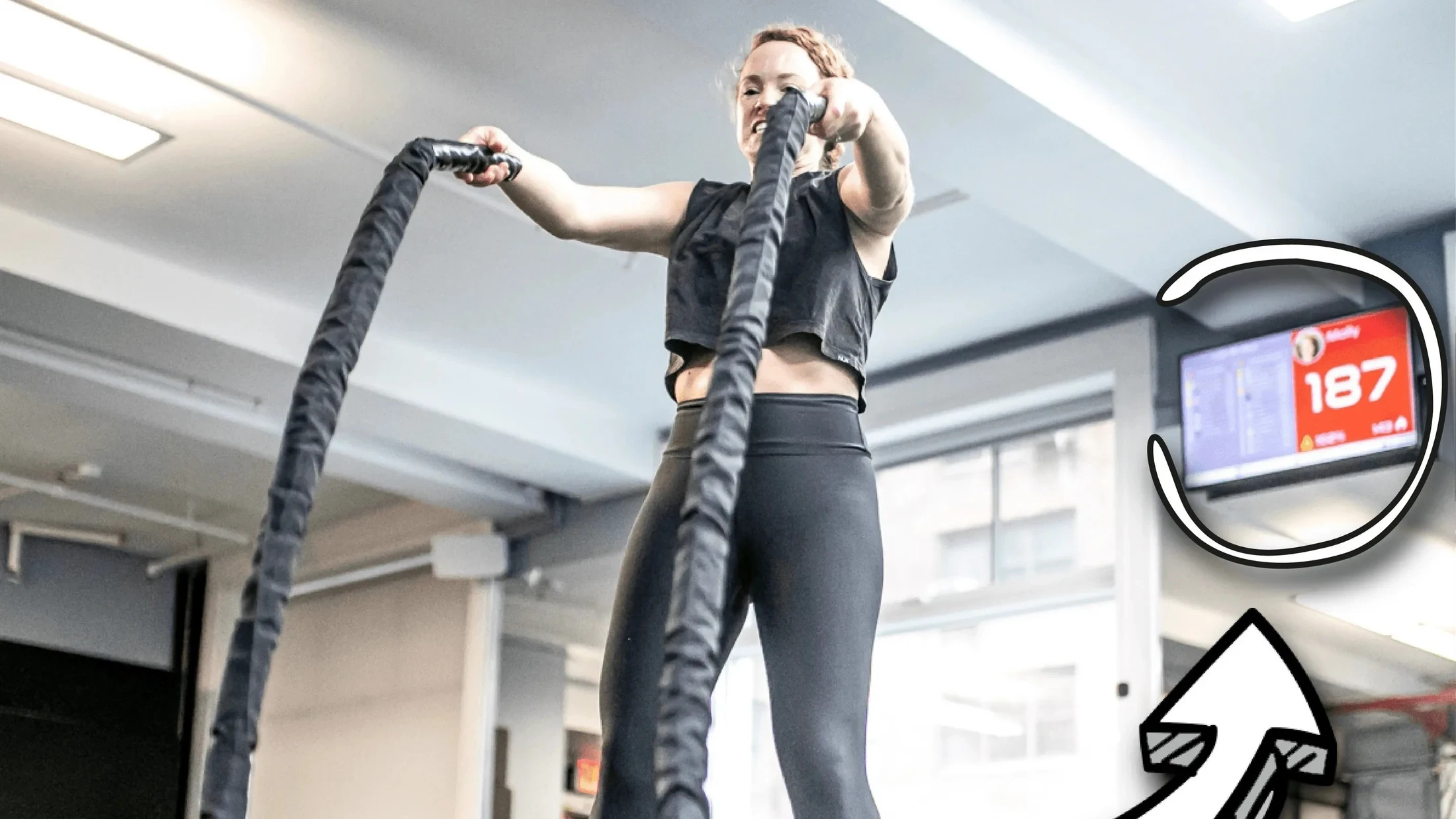 Member training with battle ropes at The Zone NYC while heart rate appears on the Uptivo screen