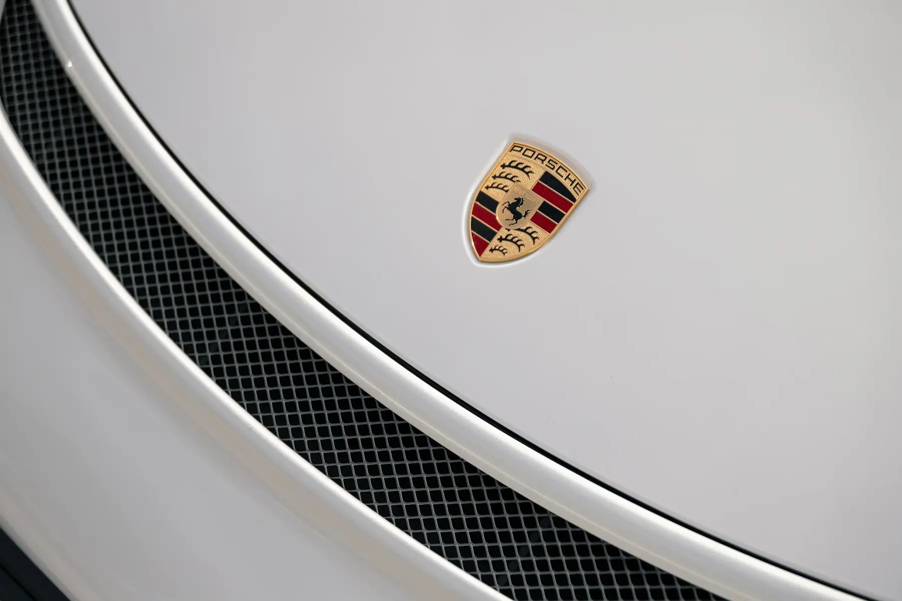 Logo Porsche sur capot blanc avec grille d’aération noire en premier plan