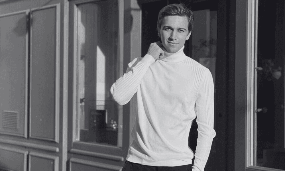 Minimalist profile shot of a man with long braids and a white shirt, set against a soft, light background.