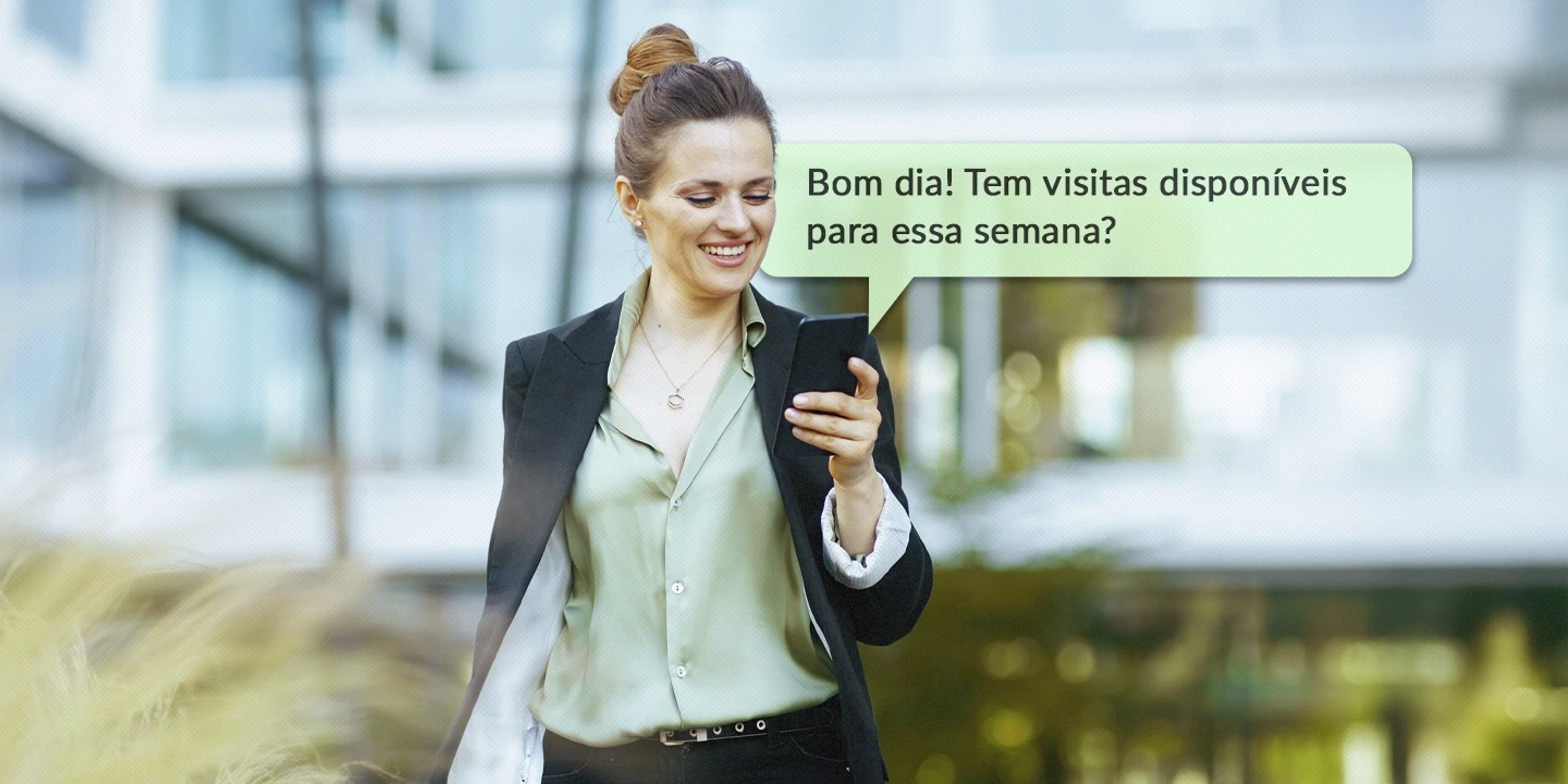 Corretora de imóveis sorrindo enquanto olha para o celular, recebendo uma mensagem de um potencial cliente no WhatsApp perguntando sobre visitas disponíveis