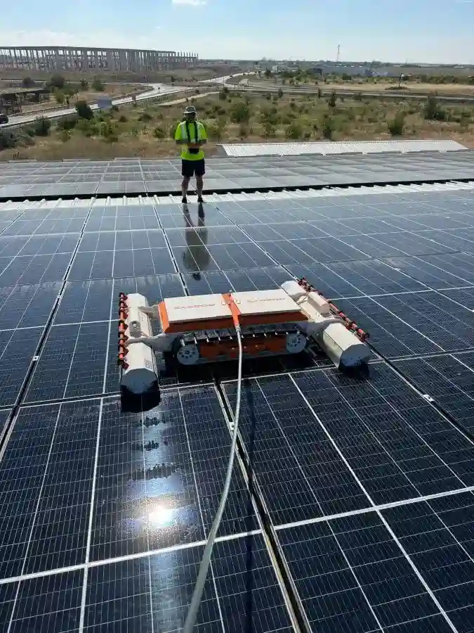 Robot de curățare SpalPanouri spălând panouri fotovoltaice pe acoperiș industrial, operat de un tehnician specializat