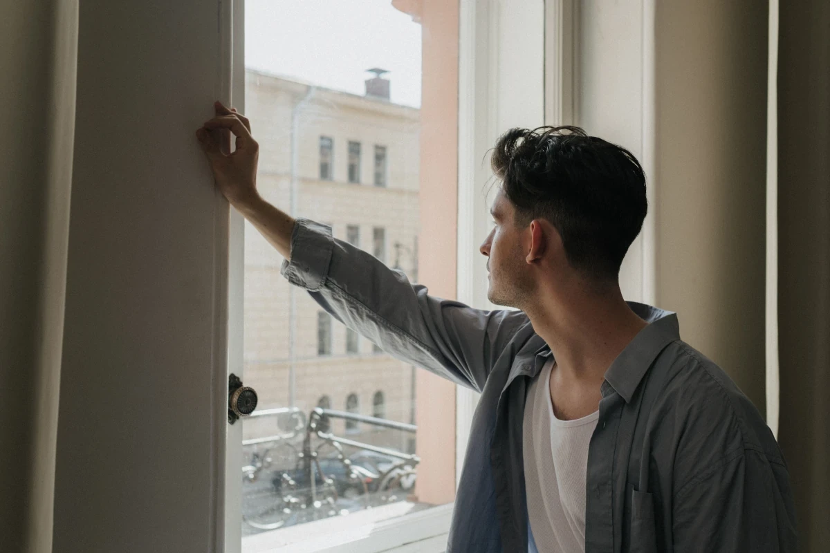 Man standing by a window, looking outside in a quiet, reflective moment.