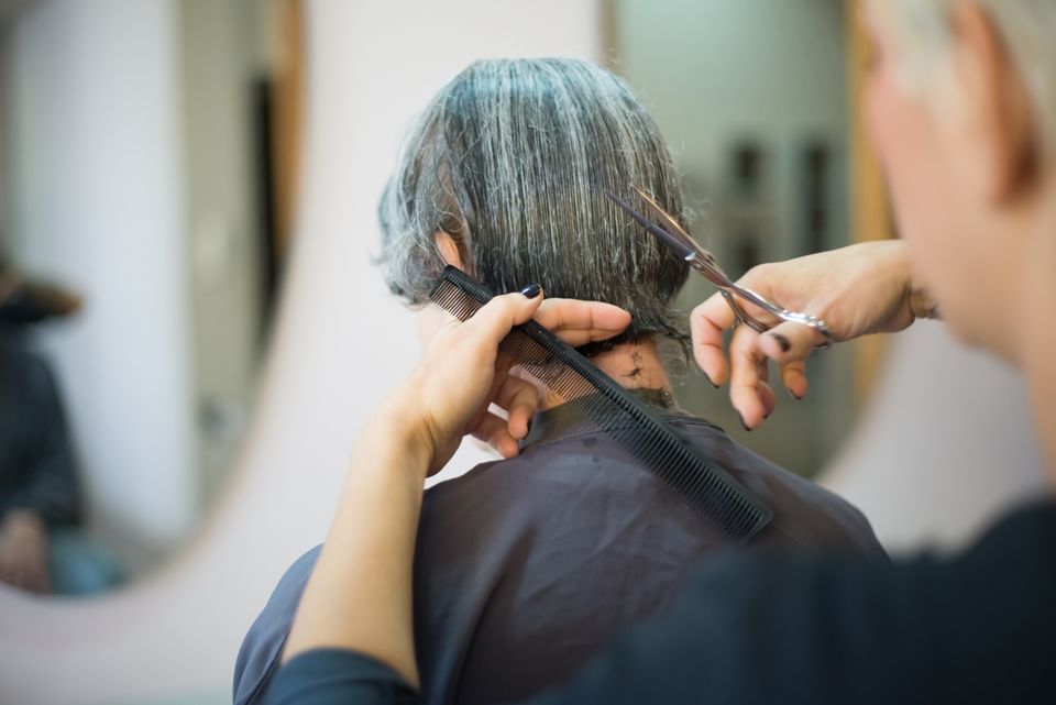 Une coiffeuse coupe les cheveux d’une cliente dans un salon lumineux.
