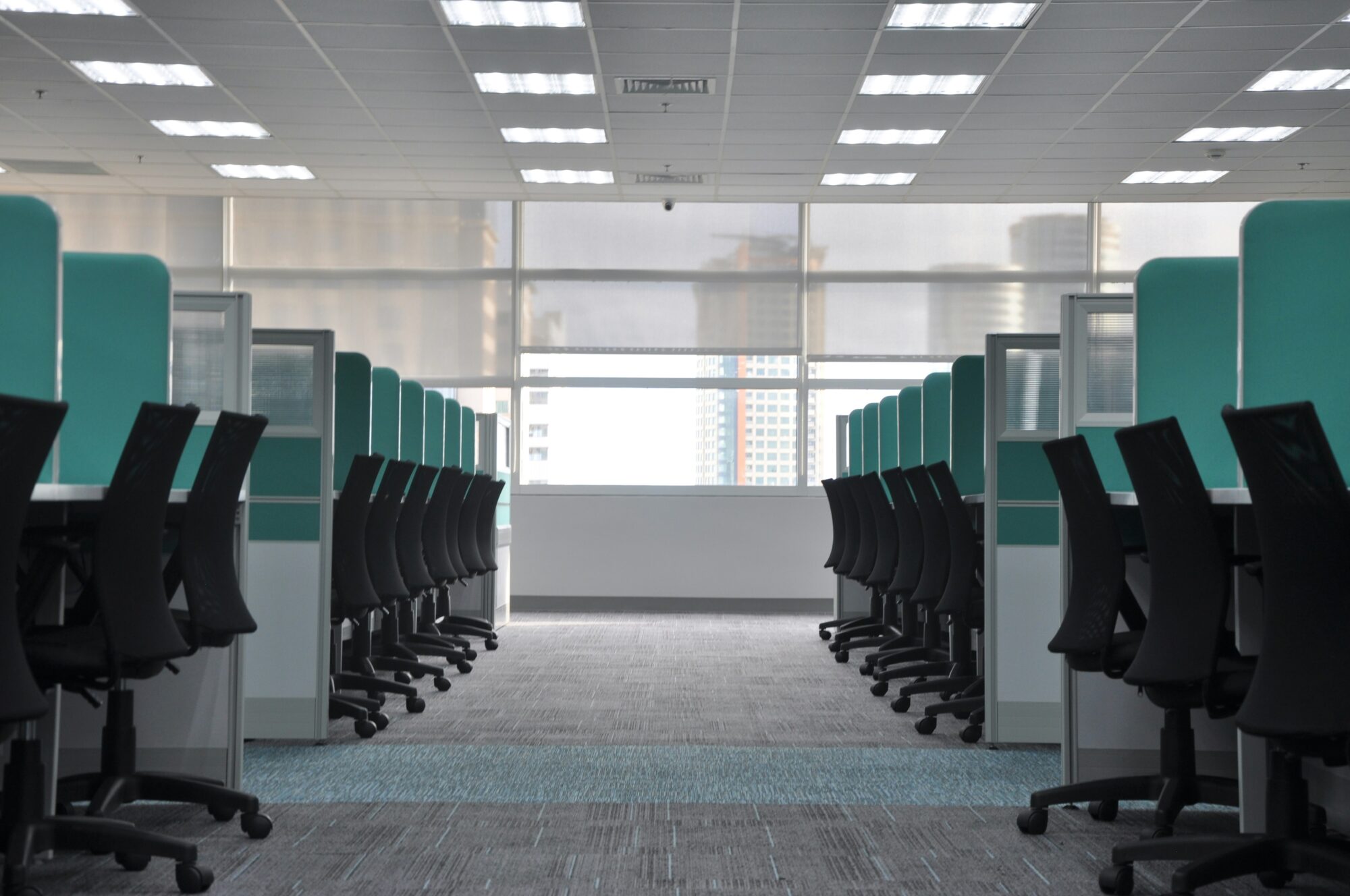 Empty office space with cubicles and ergonomic chairs, illuminated by bright overhead lights.