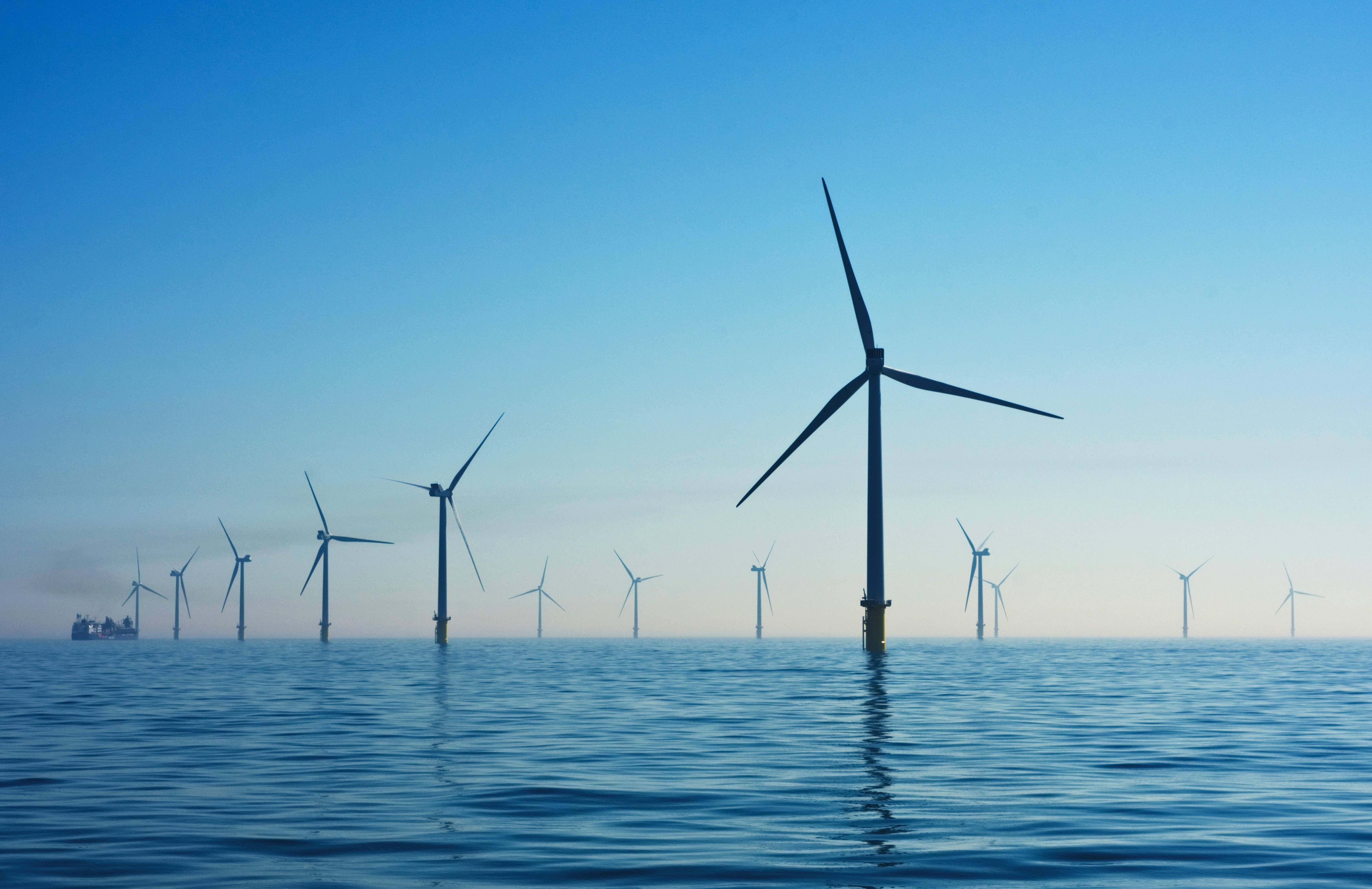 Offshore wind farm with multiple wind turbines against a clear blue sky and calm sea, conveying a sense of renewable energy and tranquility.