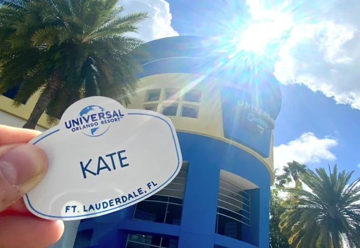 Kate holding up her Universal name tag in front of one of Universal Orlando's corporate office buikdings.