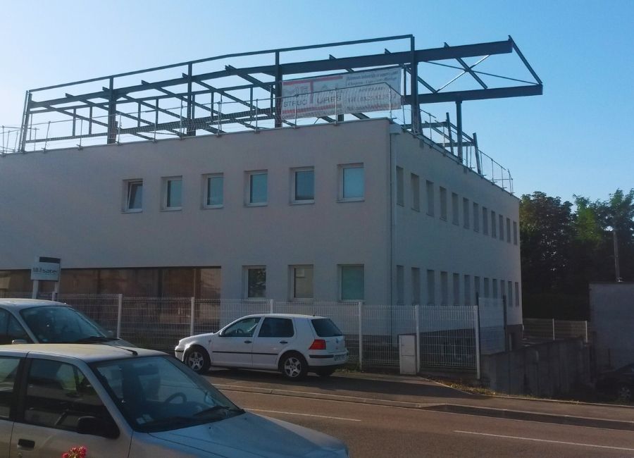 Progression du chantier métallique sur bâtiment tertiaire, avec ossature installée et façade en cours.