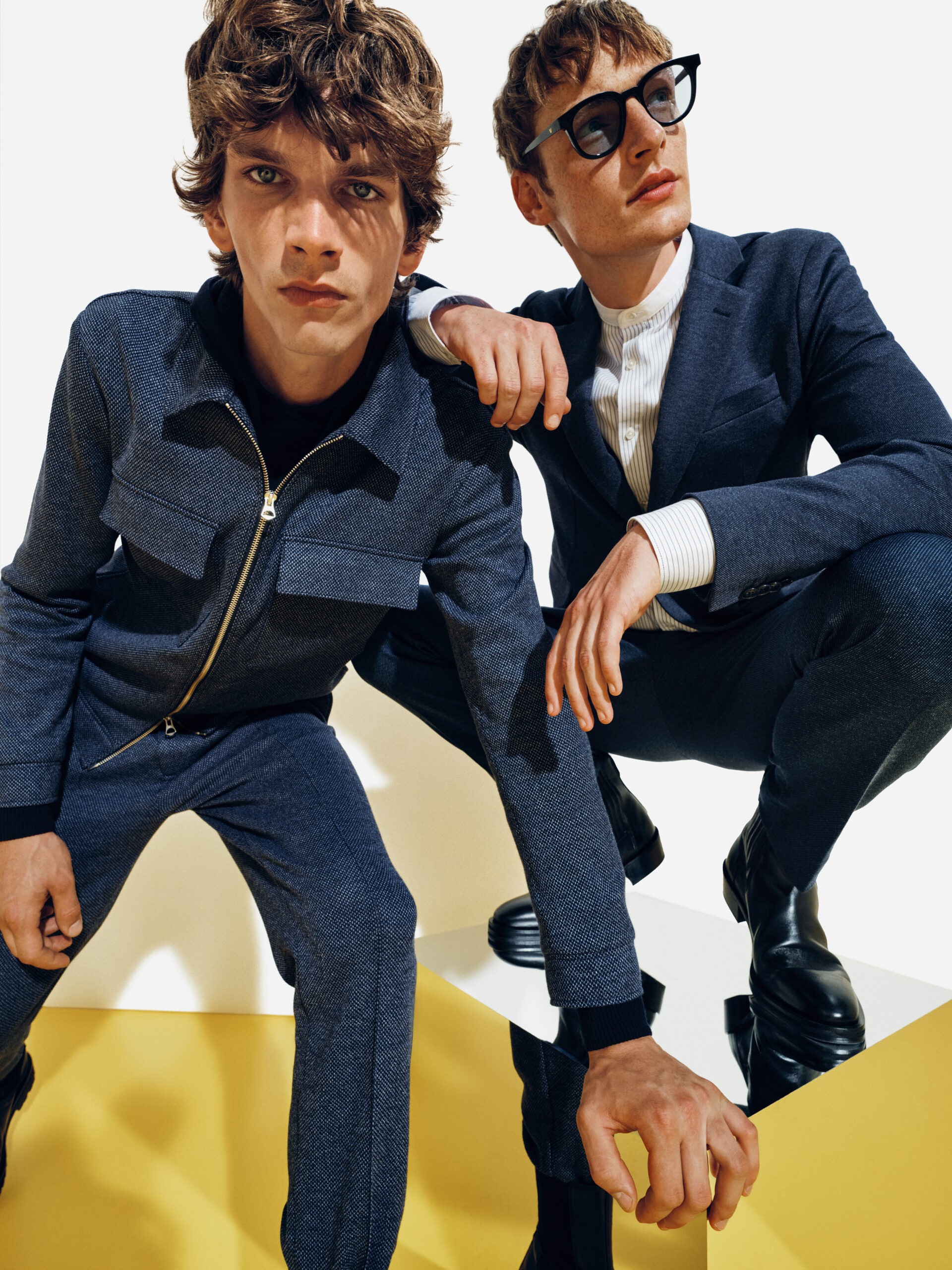 Two models in dark denim against the yellow SS22 campaign set