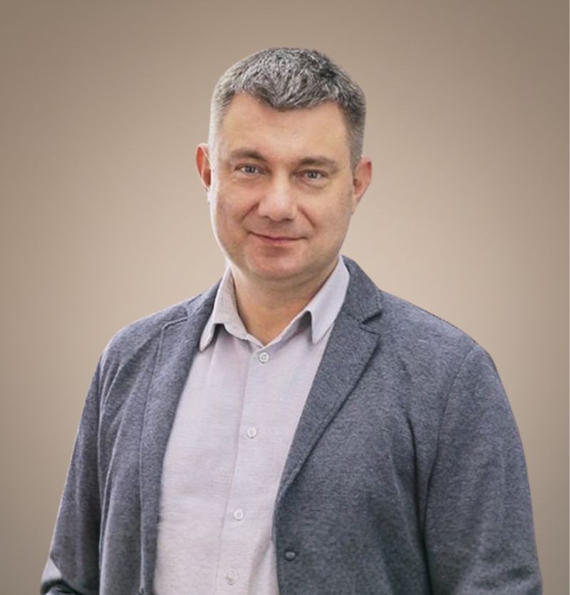 A confident person with short, styled hair and a leather jacket poses against a dark backdrop.