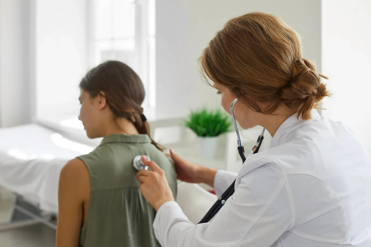 Médica examinando as costas de uma paciente com estetoscópio