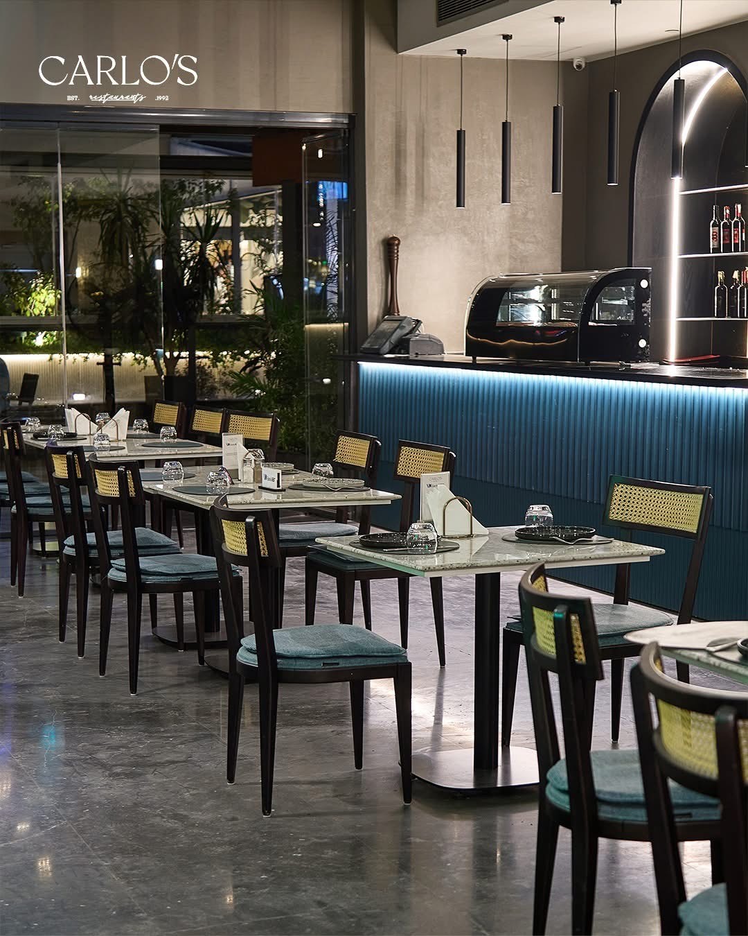 An overhead shot of a large oval plate featuring sliced, roasted duck, half glazed with a sauce, served over two thin pancakes and alongside steamed bok choy, surrounded by small bowls of condiments like scallions, sauce, salt, and carrot shreds.