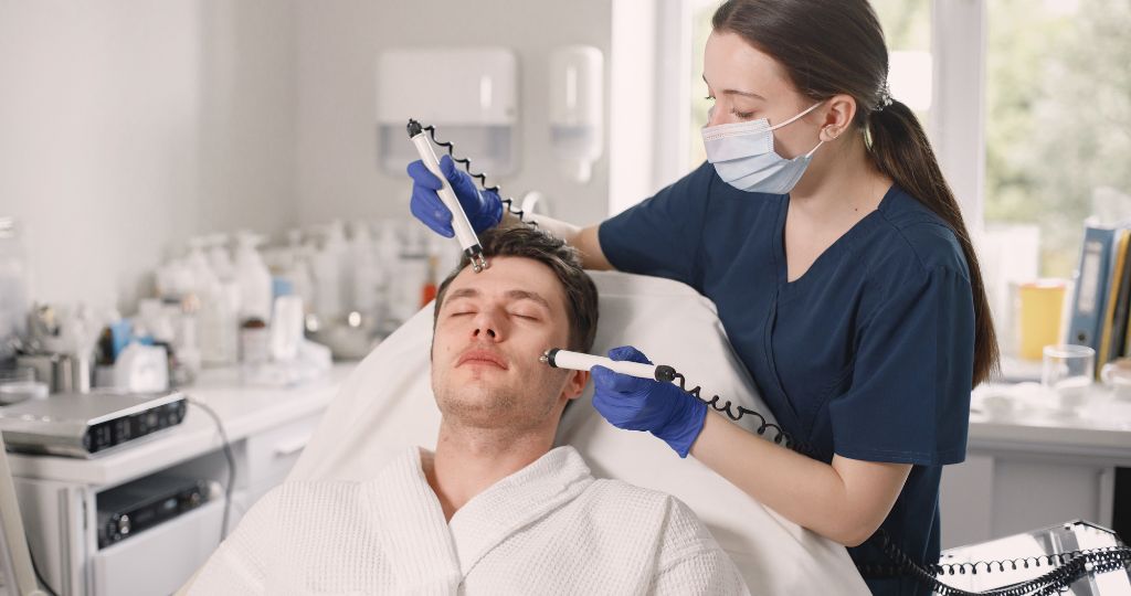 Dermatologist treats male patient in clinic with advanced skincare tools