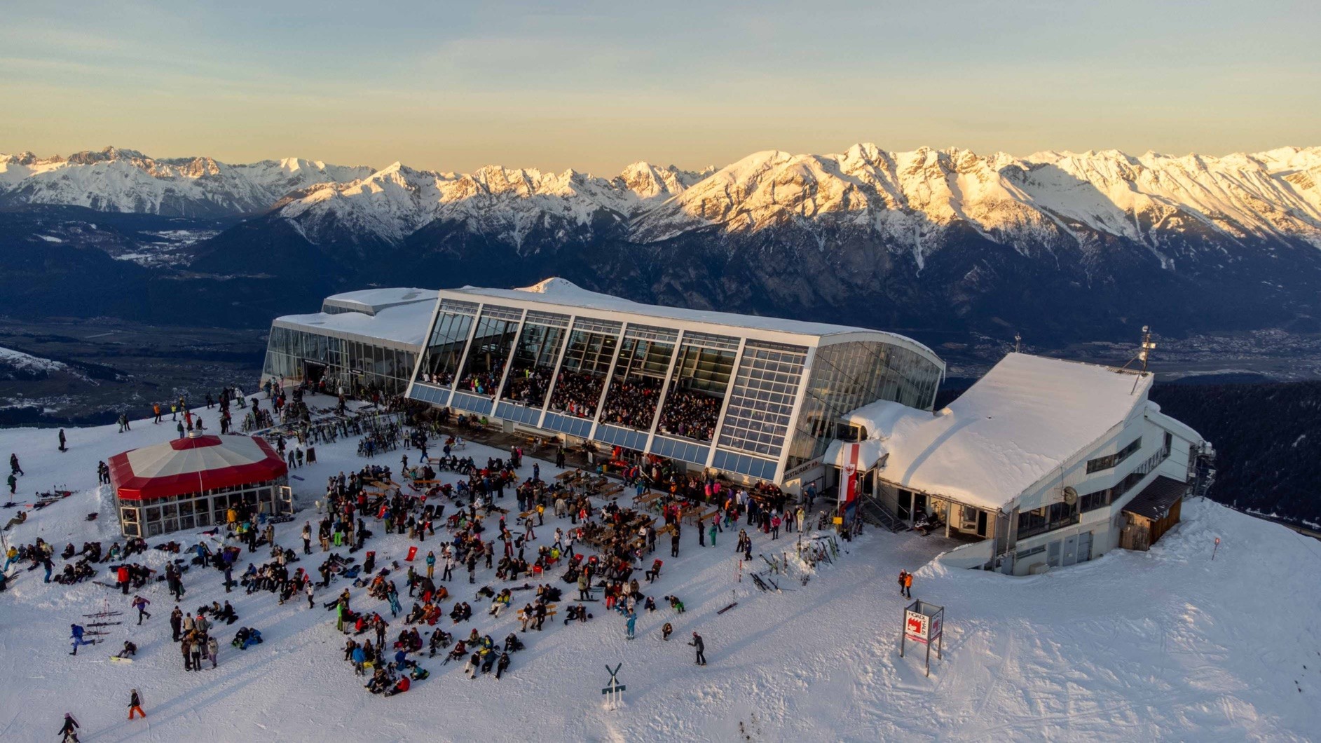 Mountain ski resort with snowy peaks, large crowd enjoying winter activities.