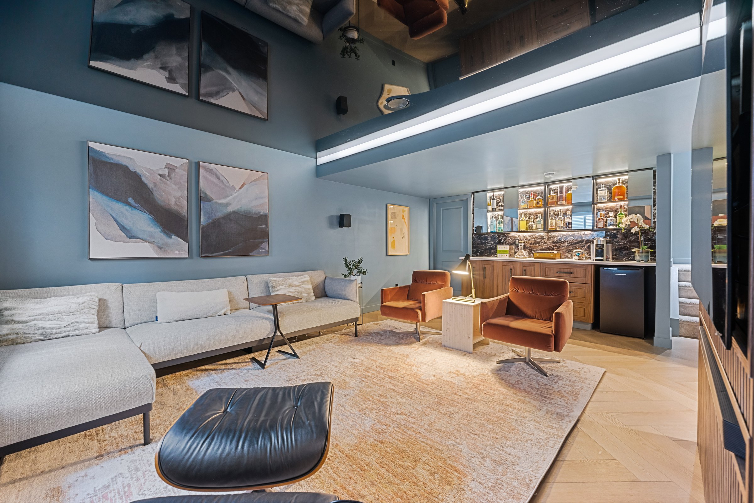 Crestmont basement finished: family room toward the lit dry bar, with cove lighting, gloss ceiling, sectional and rust lounge chairs