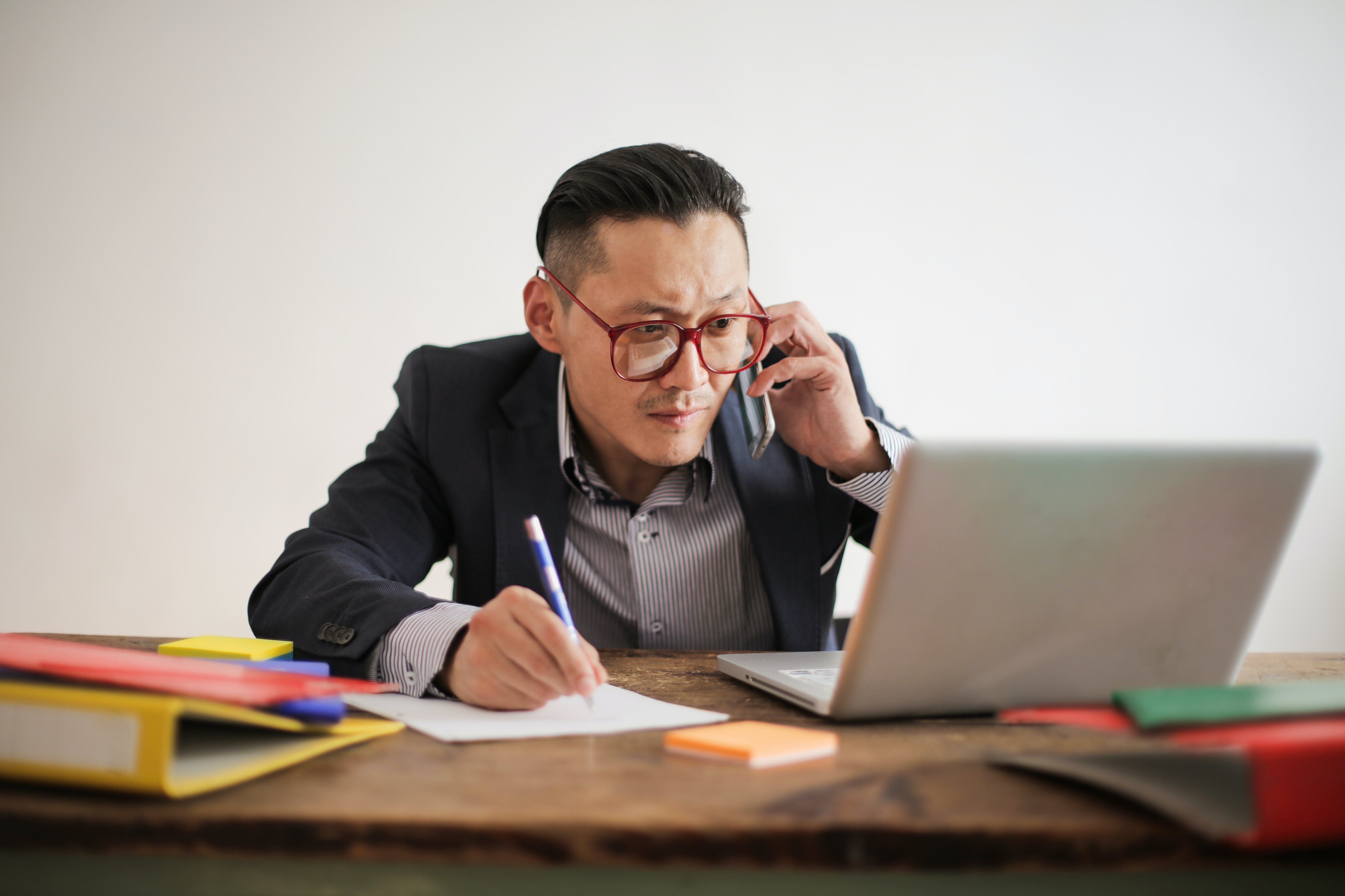 Man in black suit writing on a white bond paper preparing to contact businesses