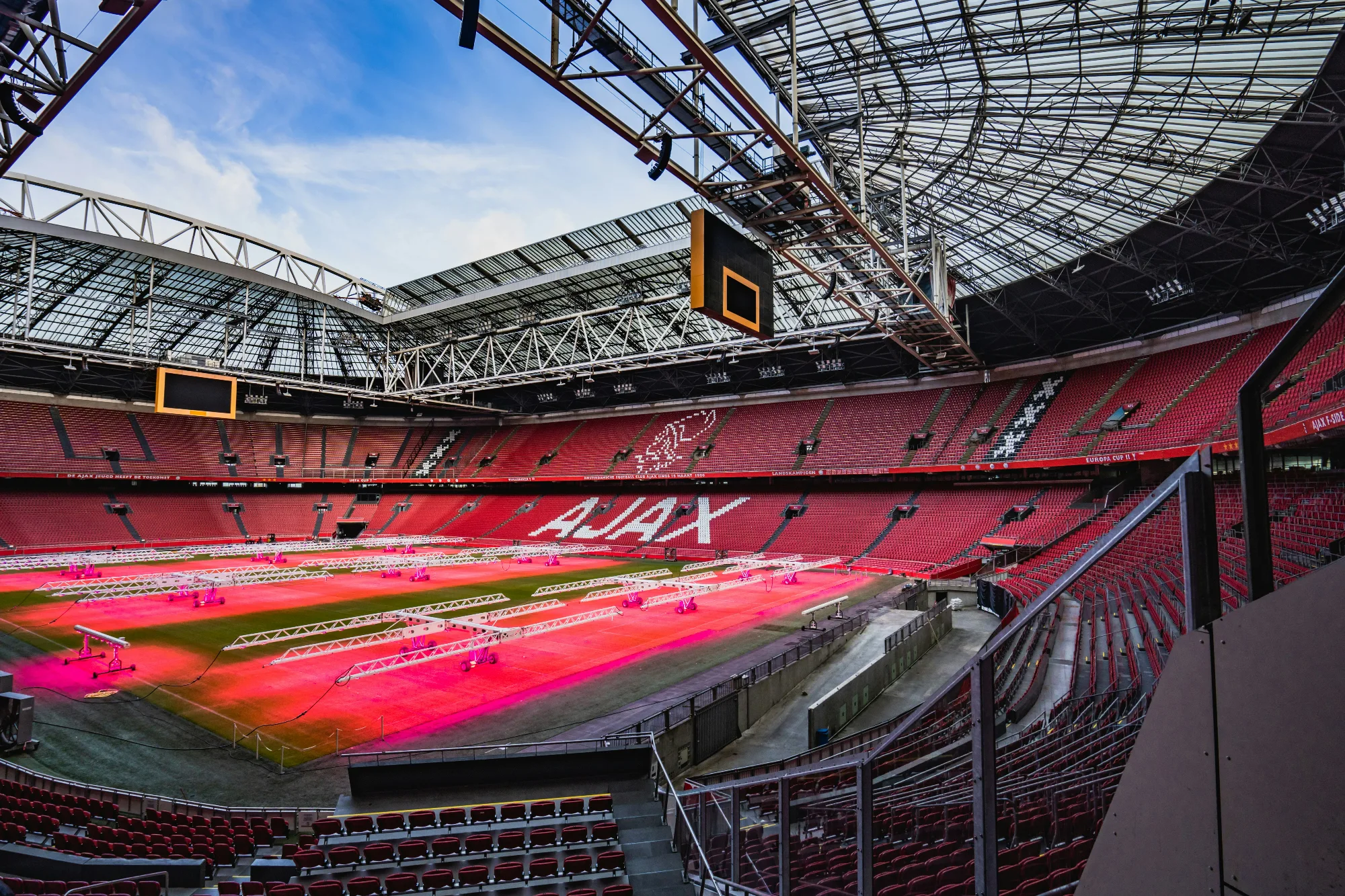 Johan Cruyff Arena, home of AFC Ajax, with red seating and illuminated pitch.