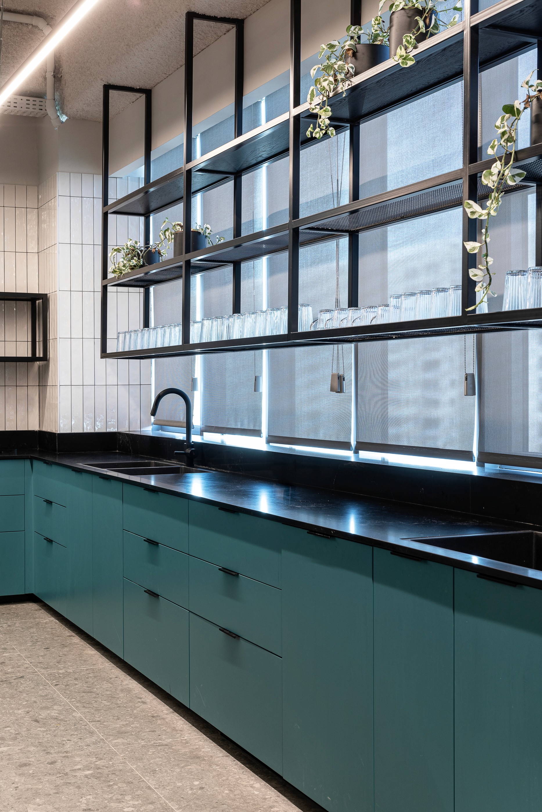 פרט עיצוב במטבח: שילוב חומרים בין קרמיקה מזוגגת בגוון ירוק עמוק, משטחי עבודה איכותיים ומדפי עץ פתוחים לאווירה קלילה.