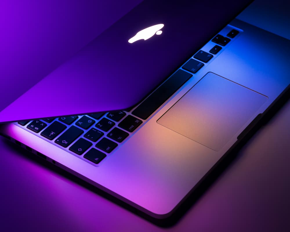 A macbook laptop halfway closed with a neon purple background