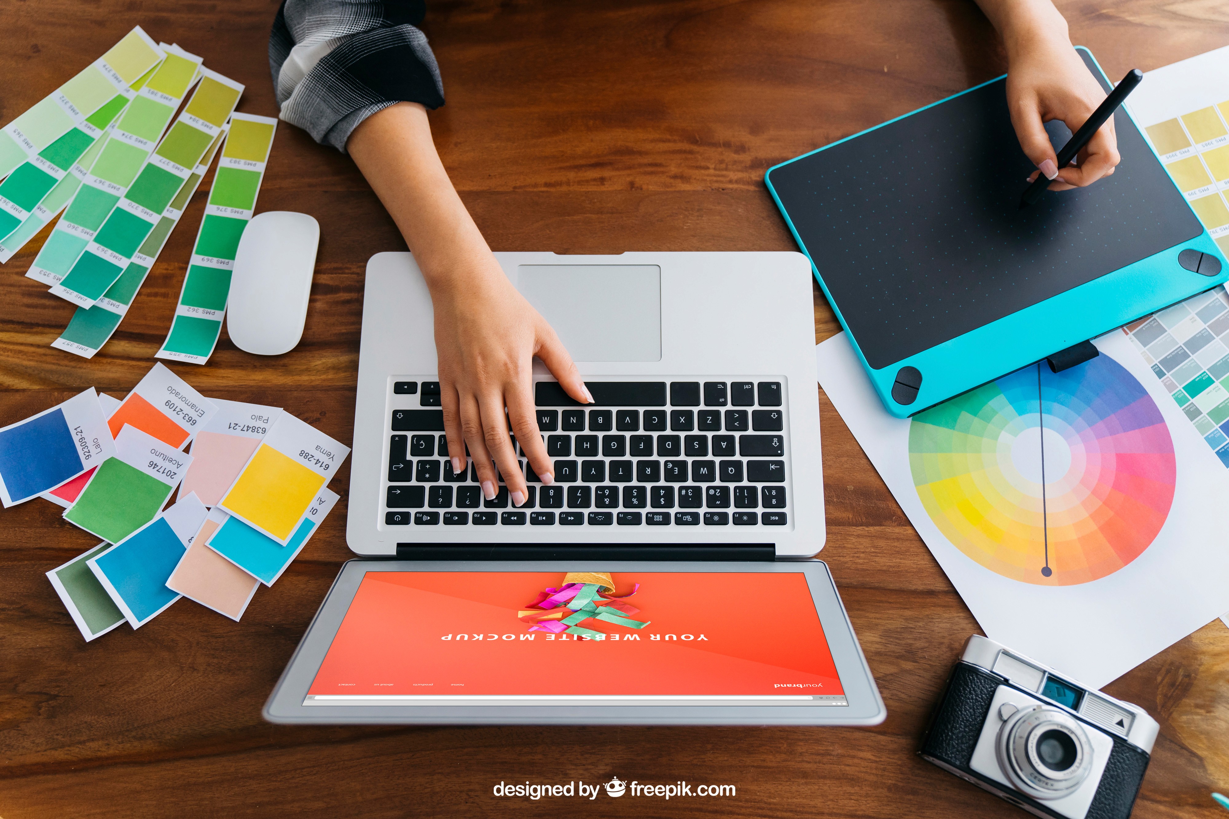 Graphic design workspace with laptop, drawing tablet, color palettes, and creative design tools on a wooden desk
