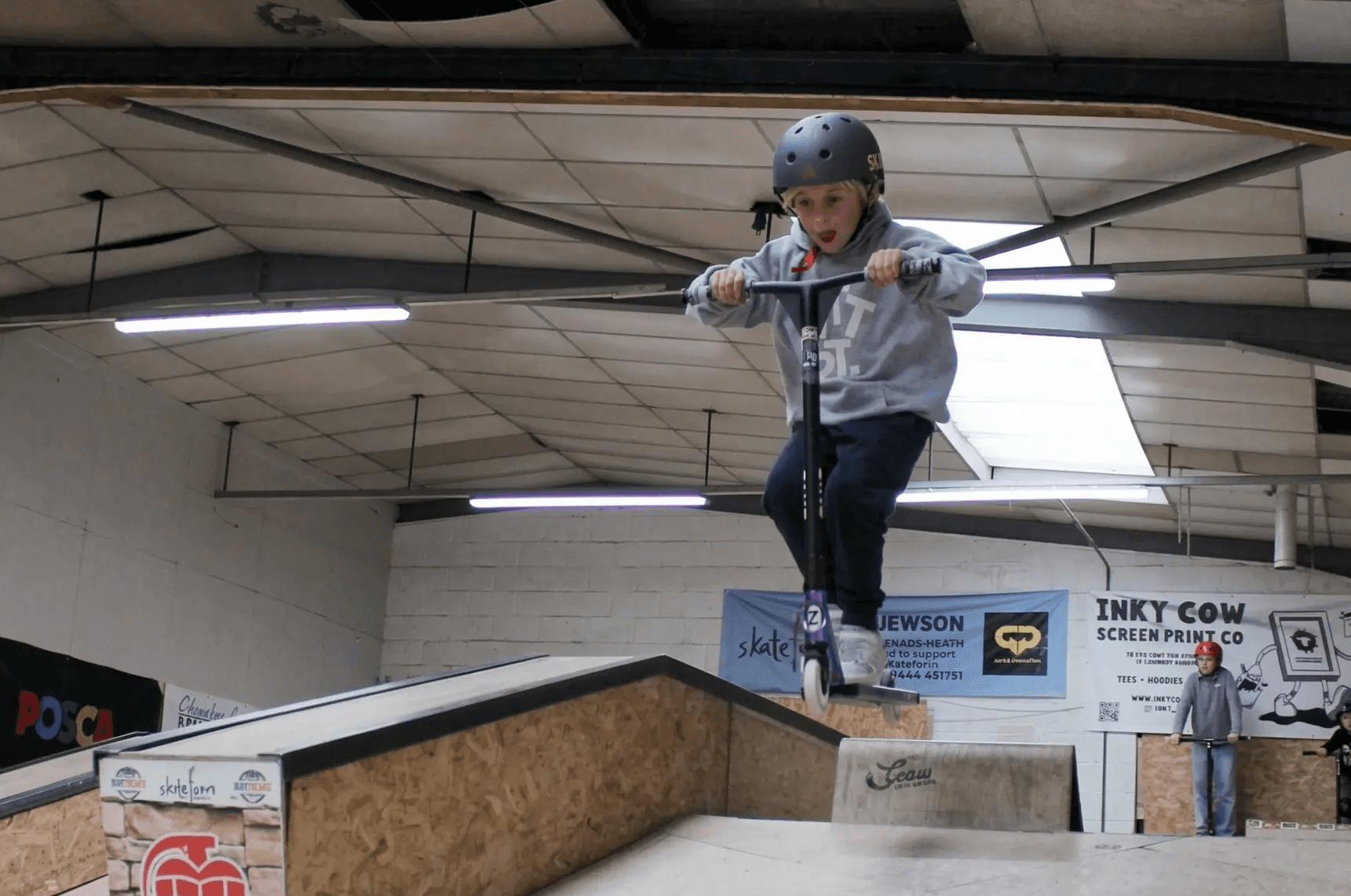 A young rider performing a scooter trick on the ramp at The Skate Farm indoor skatepark in Haywards Heath, Sussex