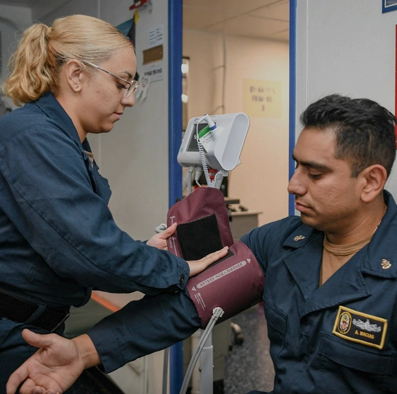 Military medical personnel taking a blood pressure reading during a clinical examination on a naval vessel
