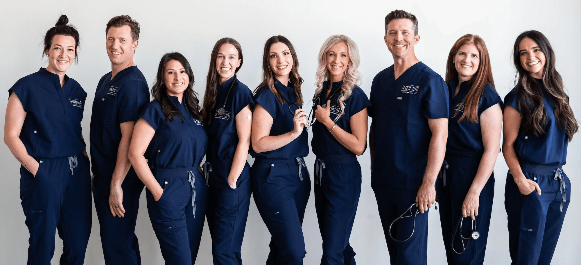 Group photo of the HRMN Health team, including Jamie Ruiz, Chelsey Galipeau, and two other employees, wearing blue scrubs in a professional medical setting.