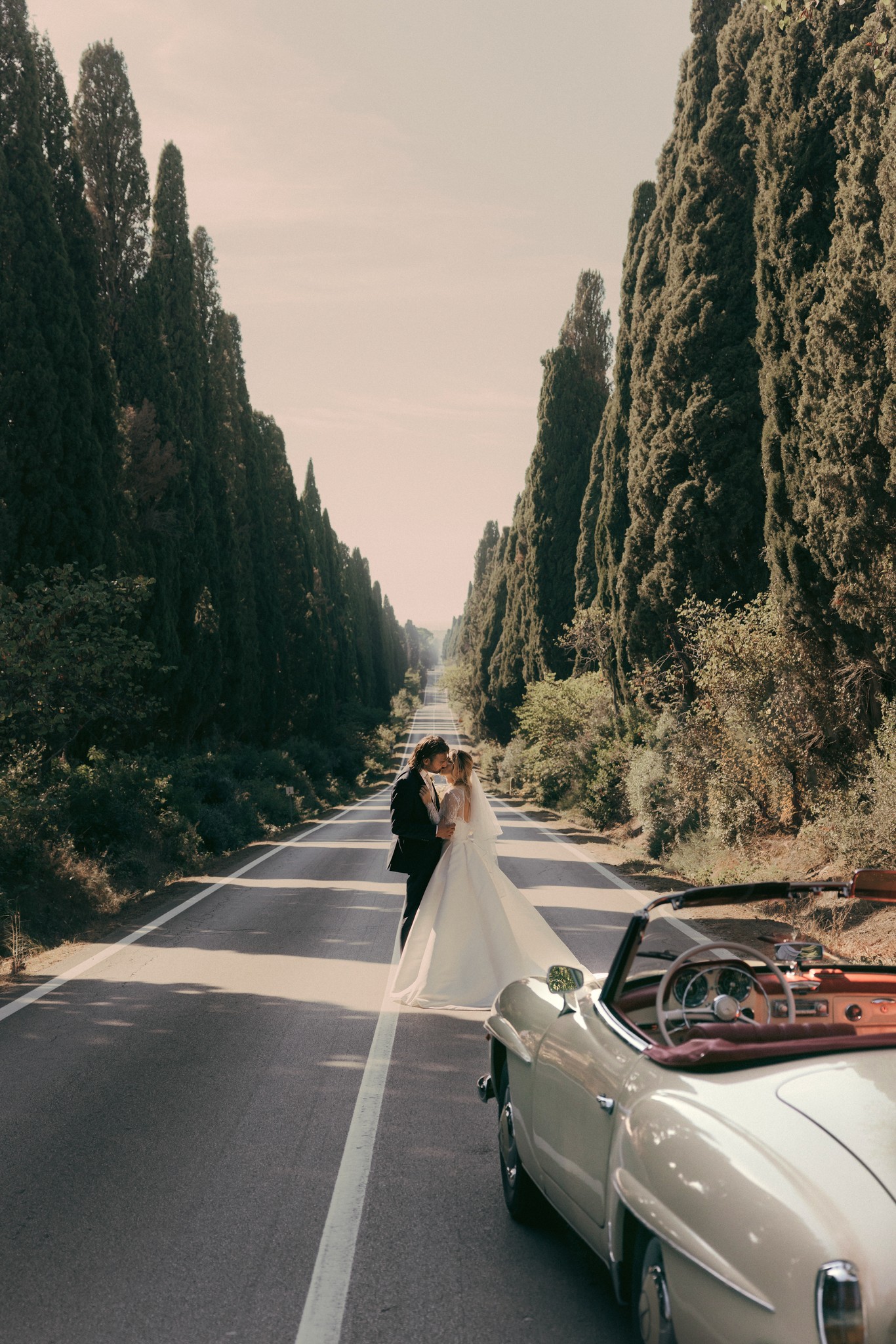 Sposi in Mercedes d'epoca sul Viale dei Cipressi di Bolgheri, abito da sposa che svolazza tra i filari toscani
