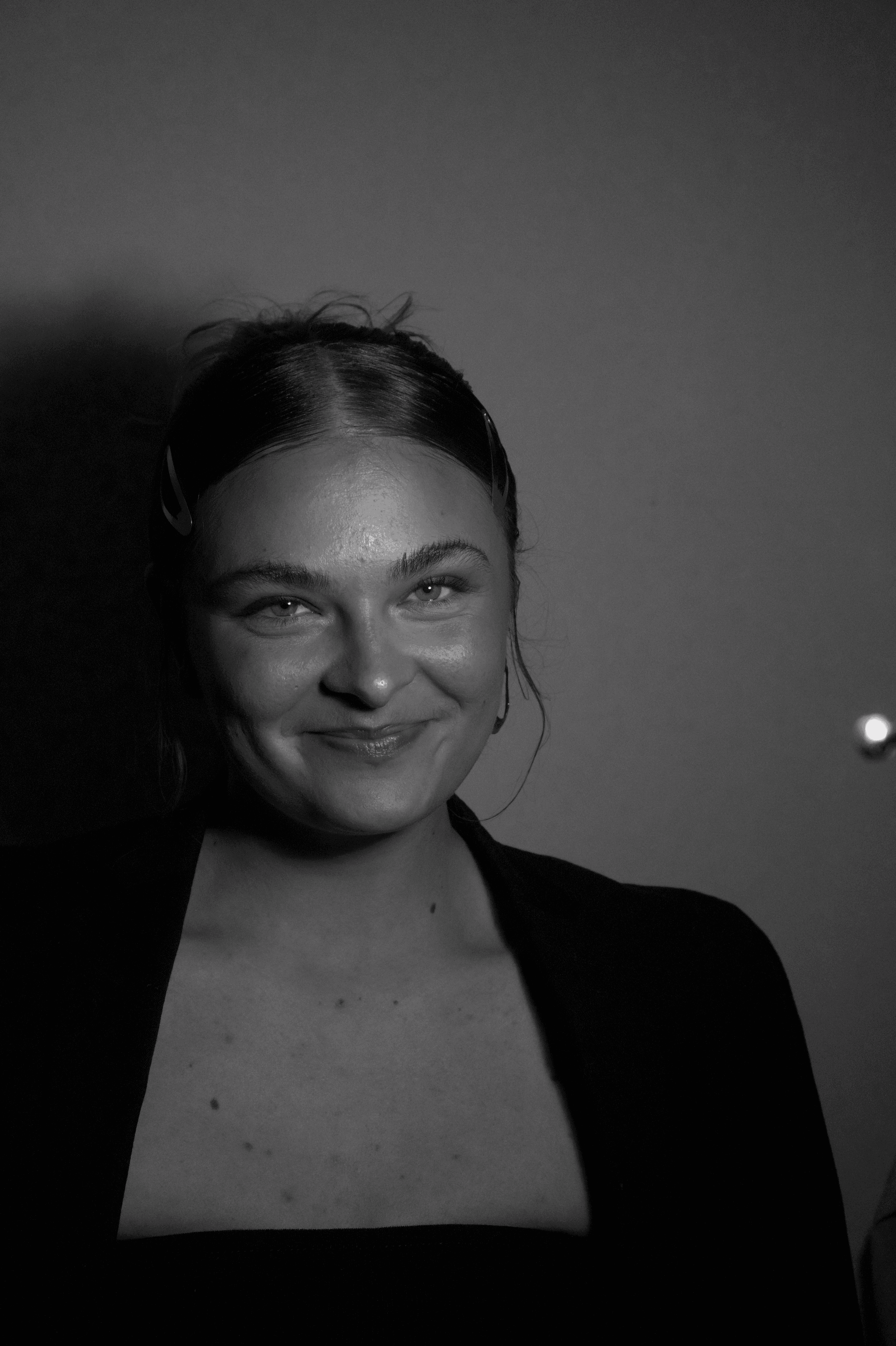 A thoughtful young person with dark hair gazes to the side, captured in soft black and white lighting.