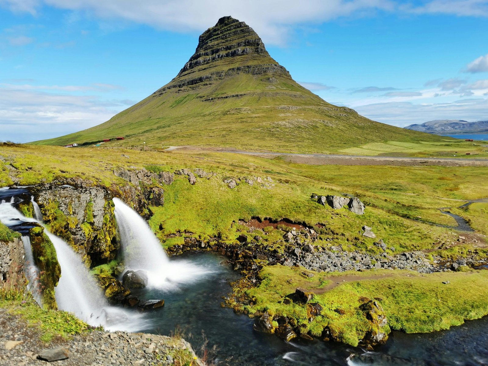 Kirkjufell mountain in green with 2 small waterfalls and clear sky on Snaefellsnes